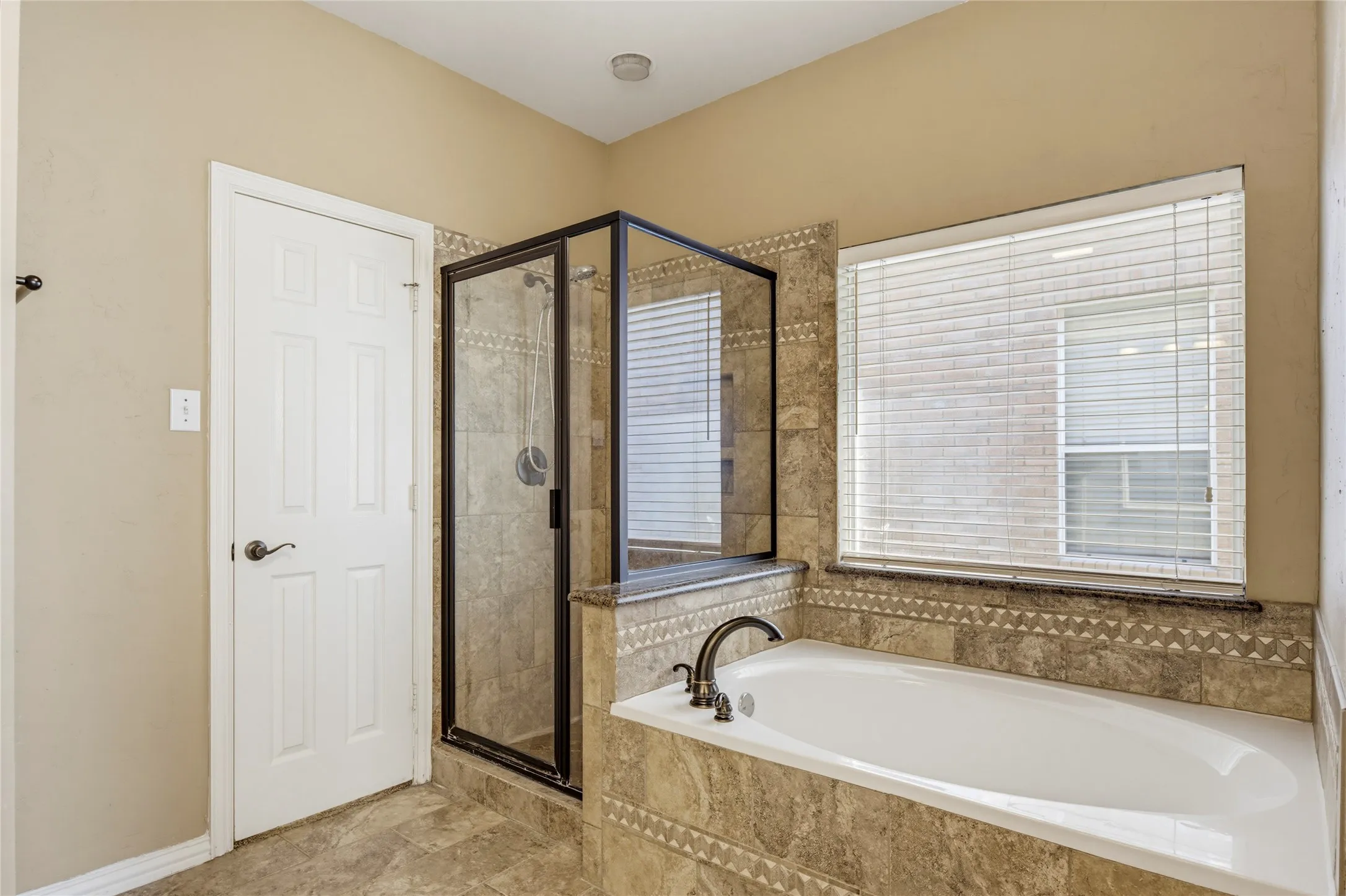 Built-in soaking tub with dark bronze fixtures, framed glass shower enclosure, and tiled surround