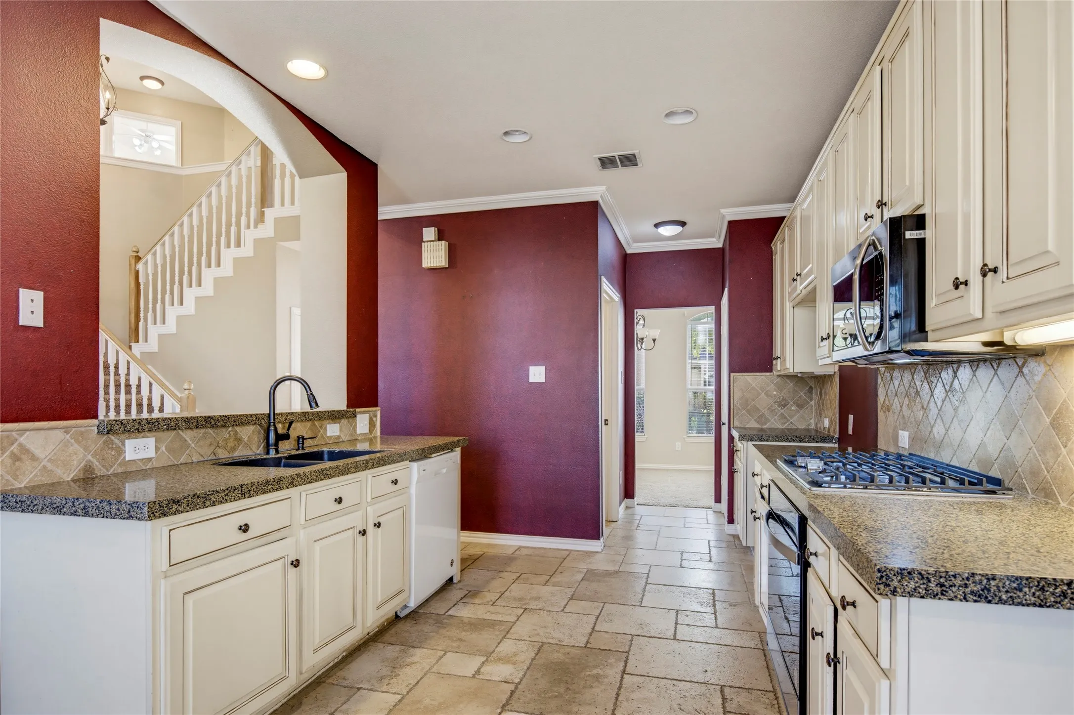 Kitchen featuring stone tile flooring, white cabinetry, integrated gas range, built-in microwave, and stone countertops