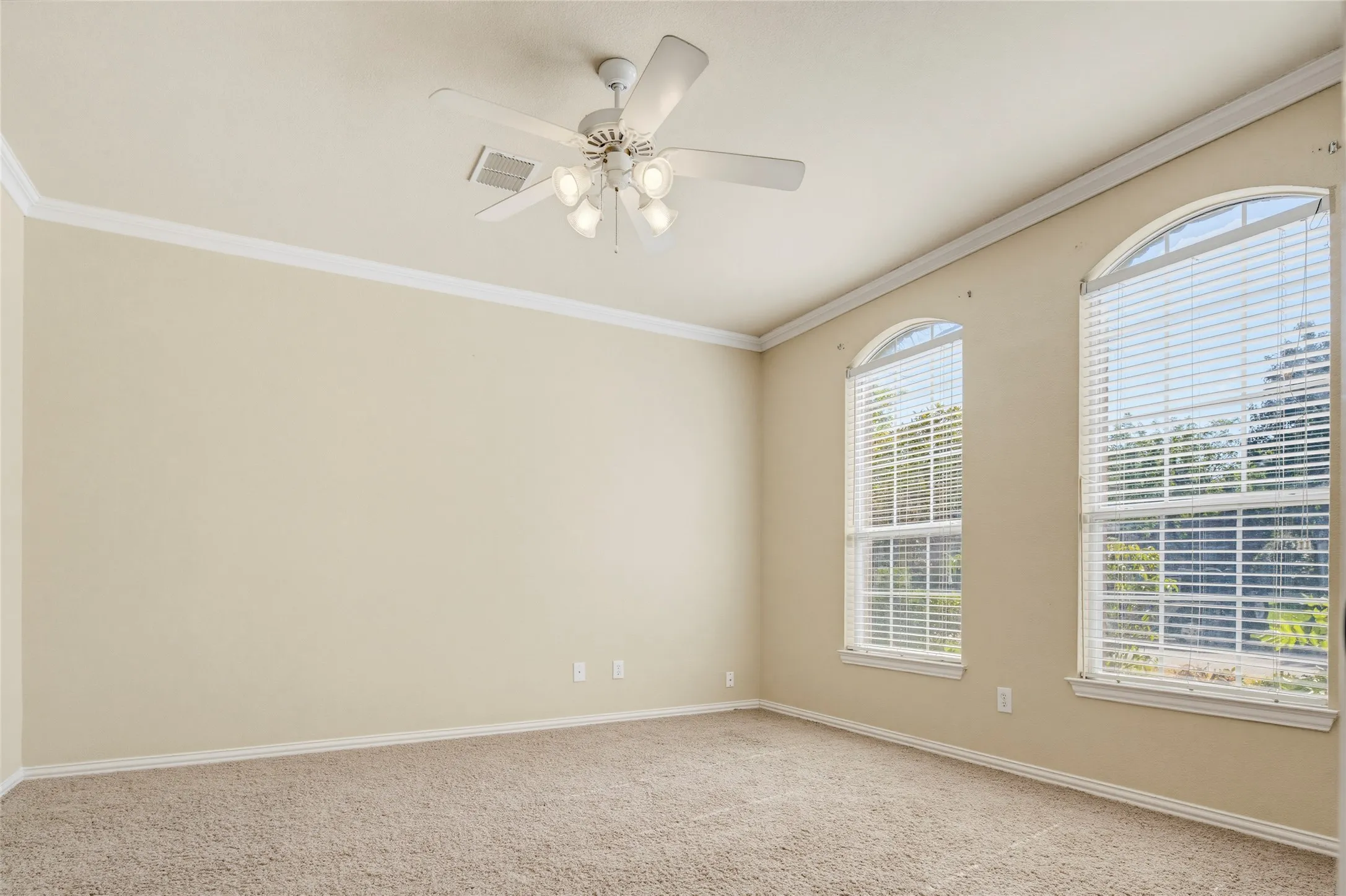 Arched windows with blinds, crown molding, ceiling fan with integrated lighting, and neutral carpet flooring