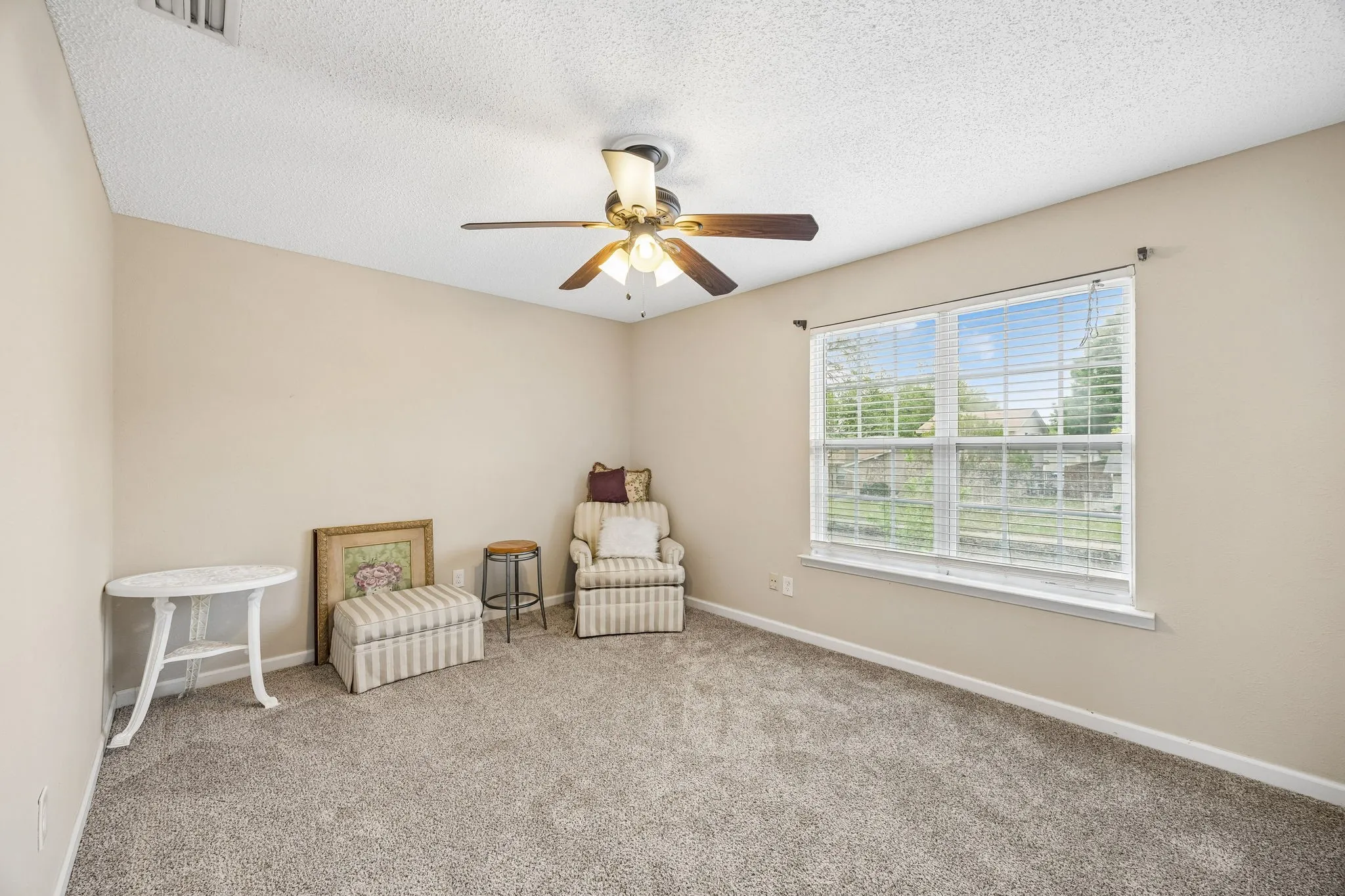 Neutral wall tones, textured ceiling, ceiling fan with integrated lighting, window with horizontal blinds, and carpeted flooring
