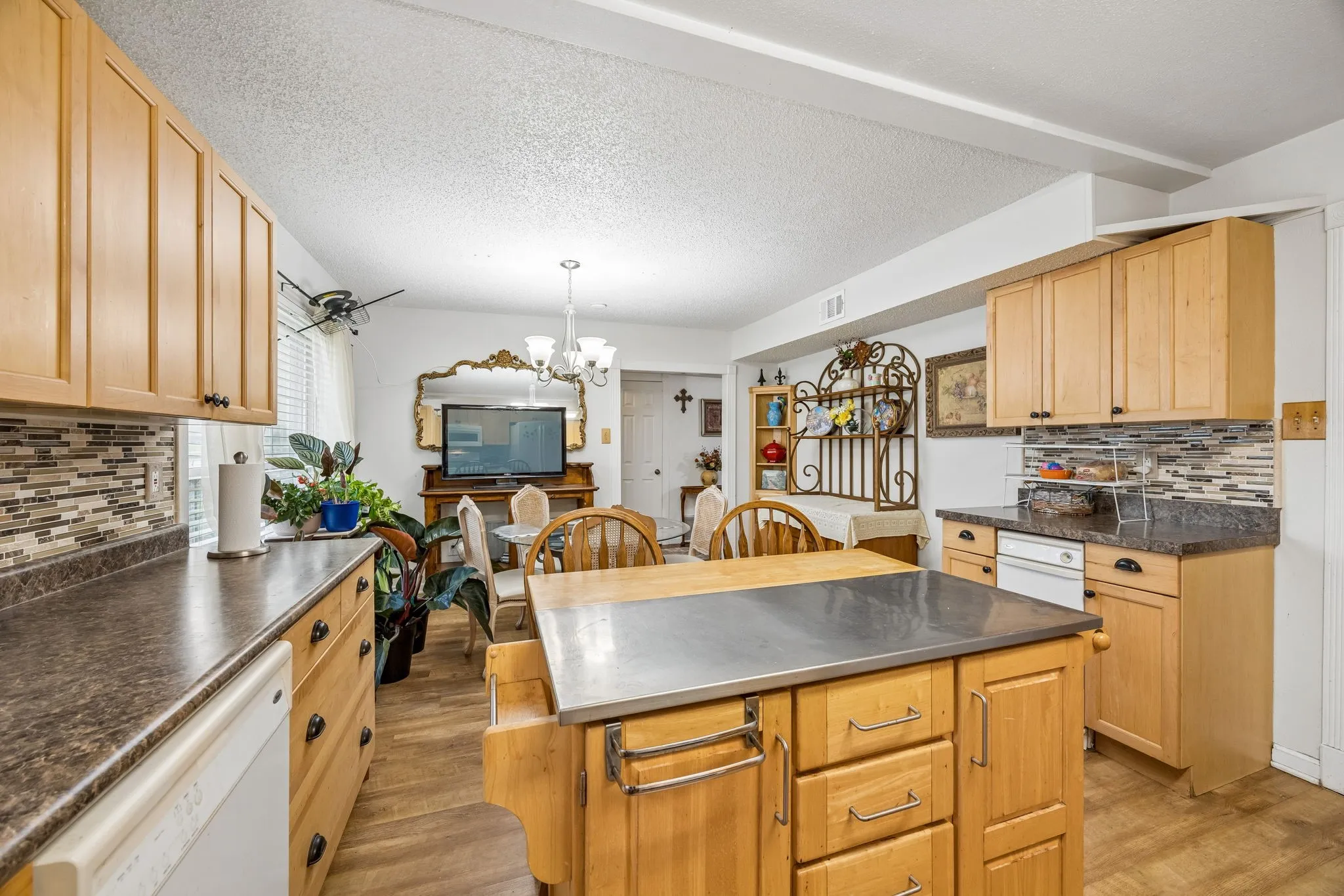 Spacious kitchen featuring natural wood cabinetry, stainless steel countertops, a large center island with storage and seating, tile backsplash, and stainless steel appliances