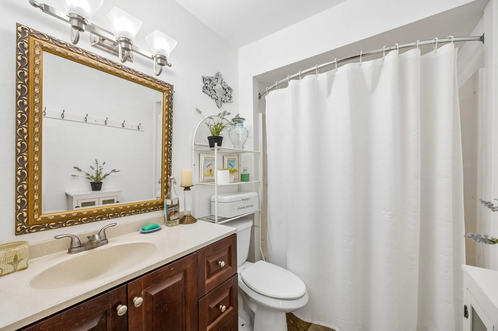 Wood-finish vanity with an integrated sink and light-toned countertop, complemented by an ornate framed mirror and a three-light fixture