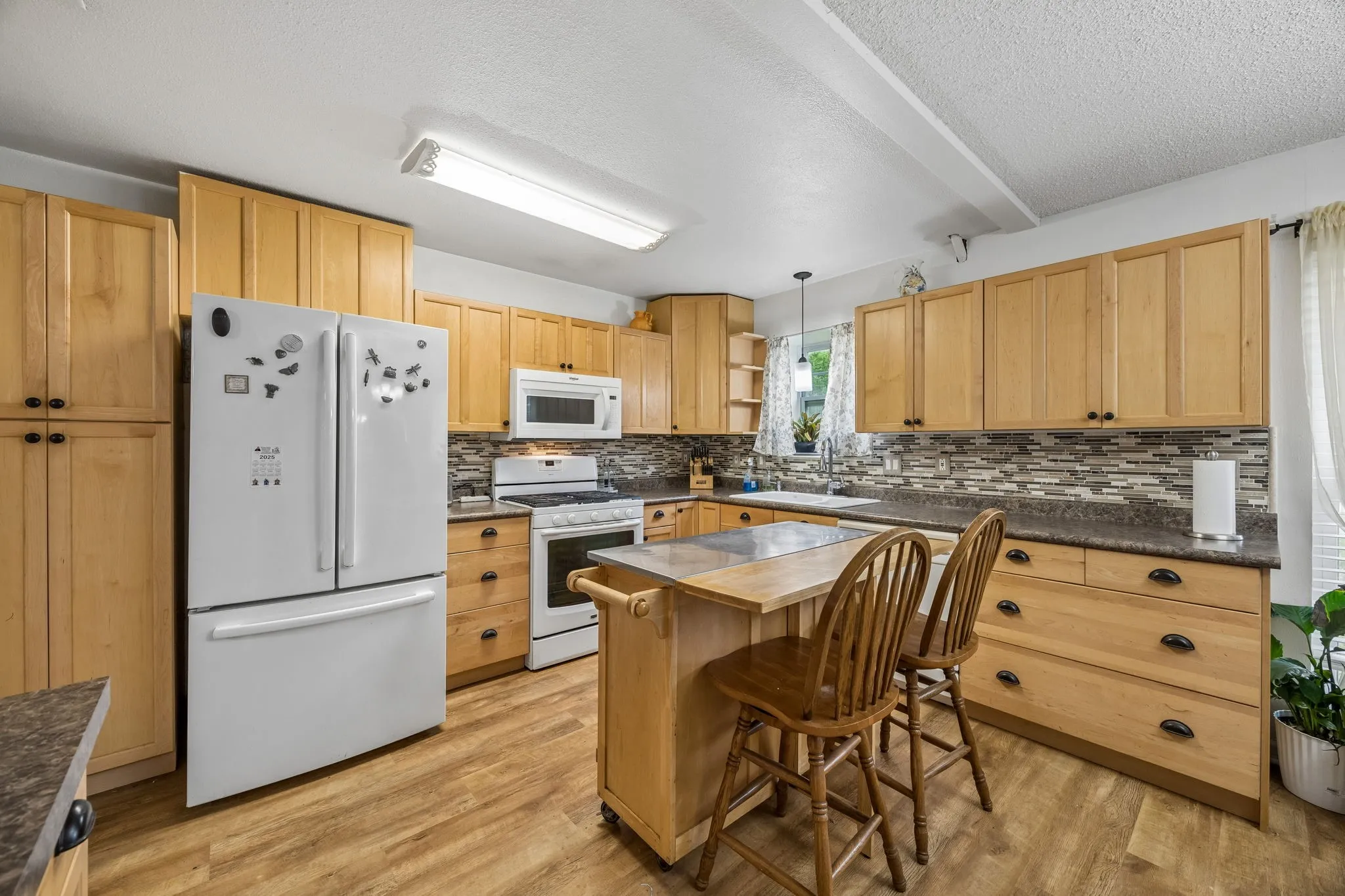 Wood-finish flooring, light tone cabinetry, white appliances, and a tiled backsplash