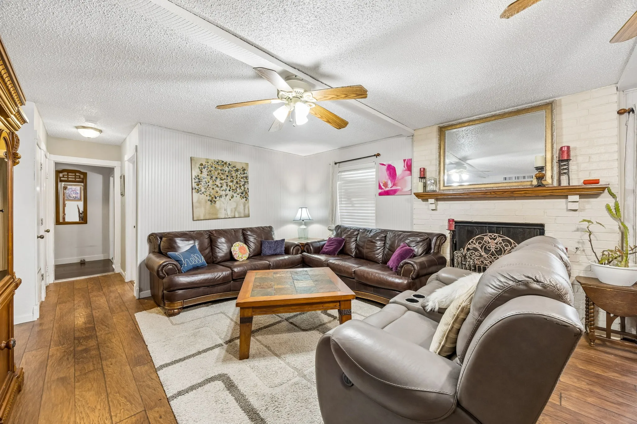 Wood-finish flooring, white brick fireplace with mantel, ceiling fans, and beadboard paneling