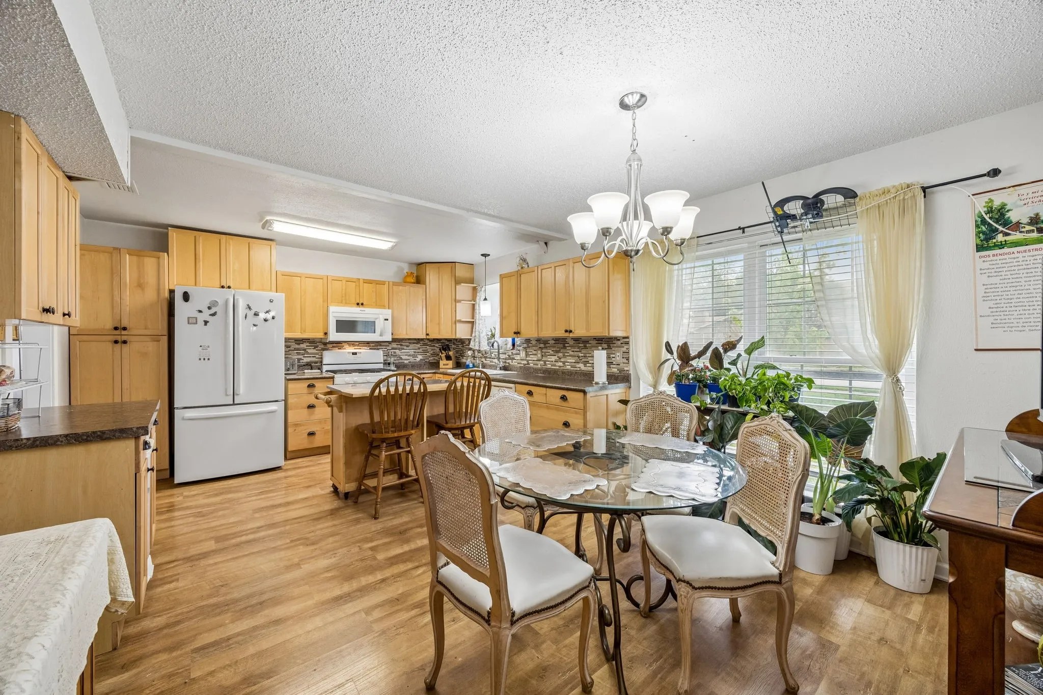 Kitchen featuring wood-finish flooring, light wood cabinetry, integrated appliances, a central island, and a dining area with a chandelier