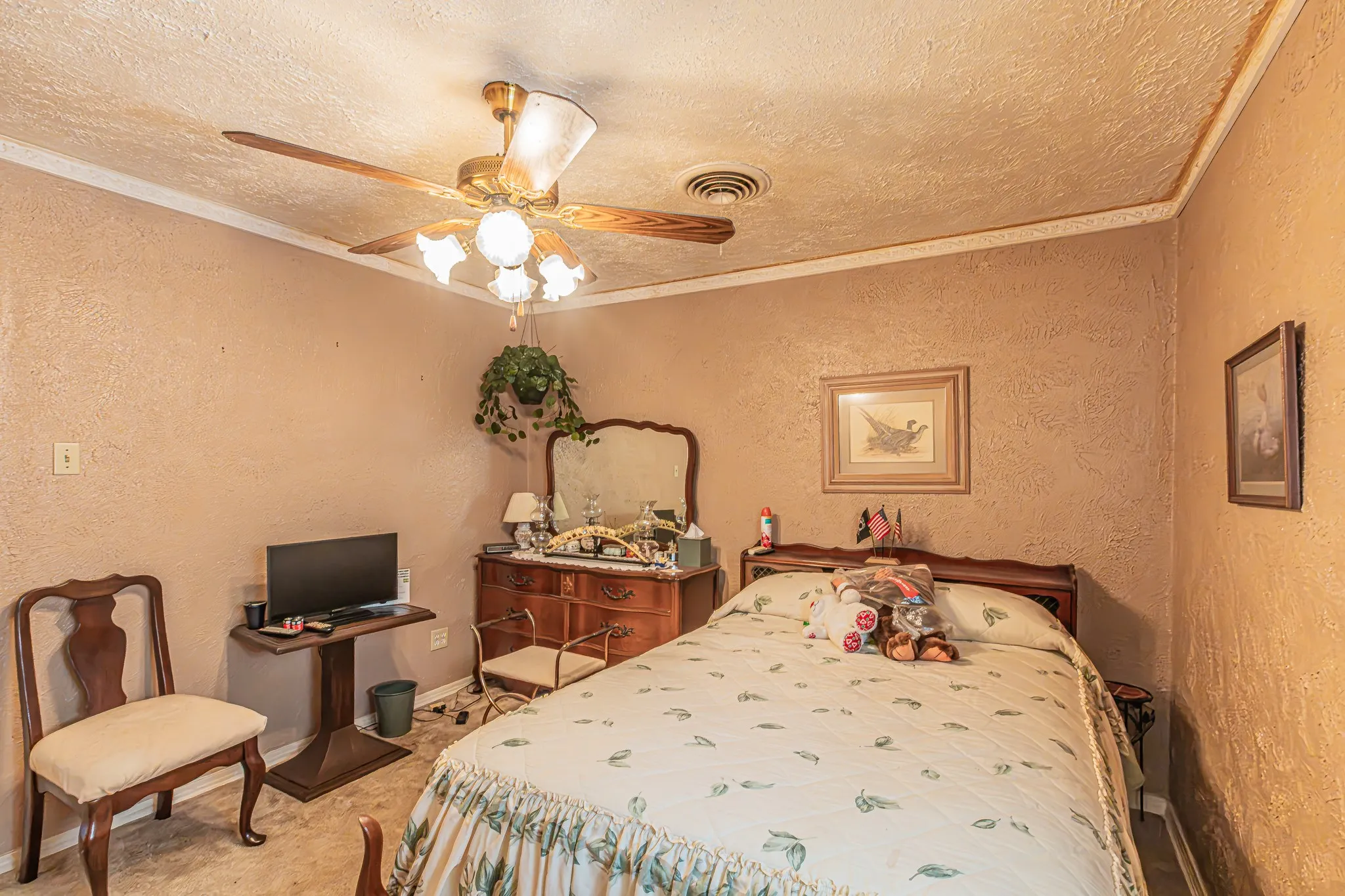 Textured wall finish, ceiling fan with light fixture, ornate crown molding, wood-finish bed frame, and built-in dresser with mirror