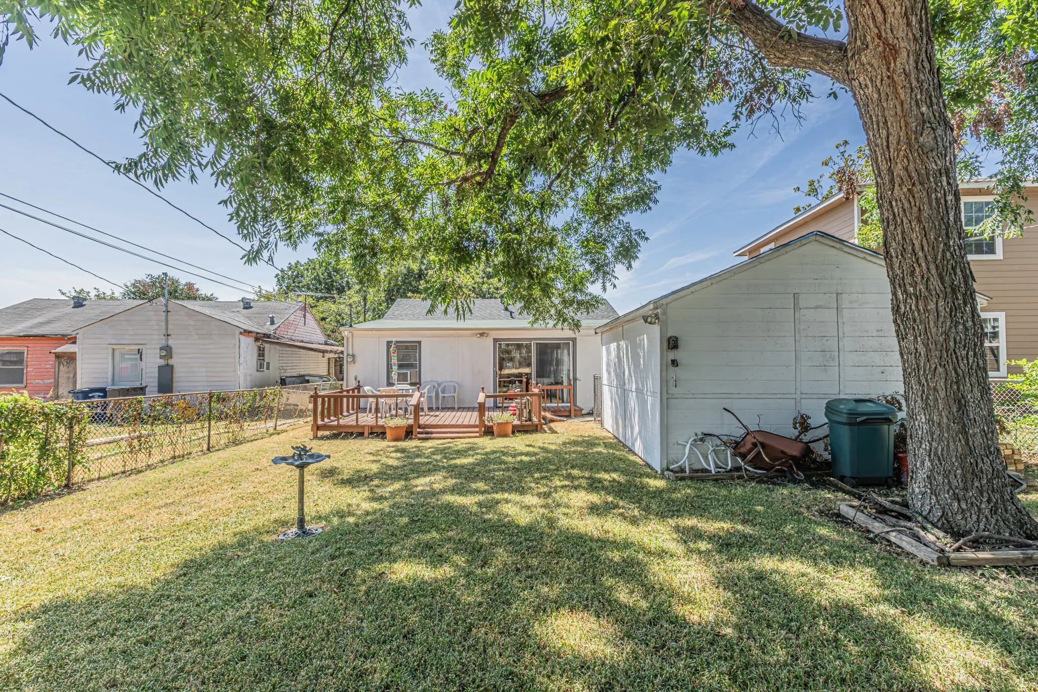 Expansive backyard featuring a wood deck, sliding glass doors, detached shed, and chain-link fencing