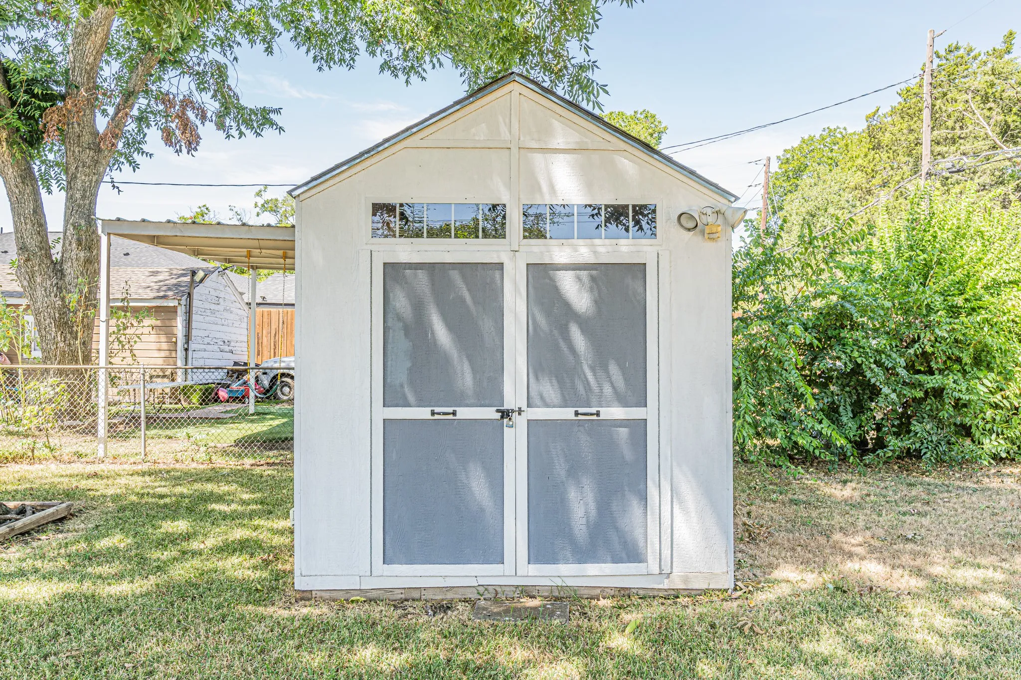White storage shed with a gable roof, transom windows, and double screen doors