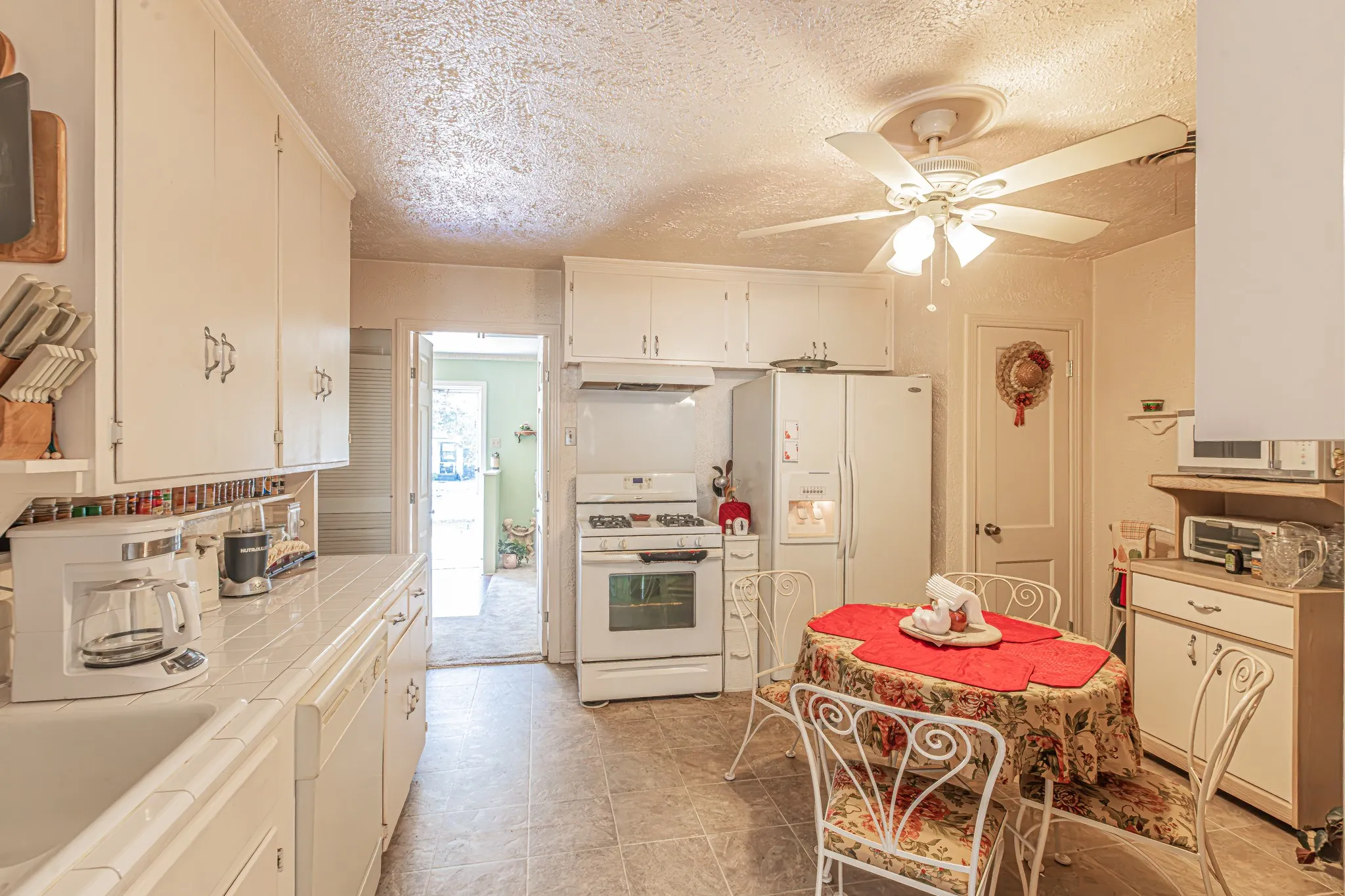 White kitchen cabinetry with tile countertops, integrated sink, tile flooring, and ceiling fan with integrated lighting
