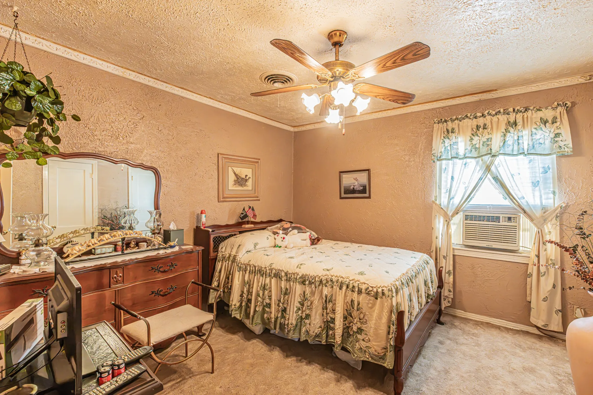 Textured walls with crown molding, ceiling fan with light fixture, window with an integrated air conditioning unit, and carpeted flooring