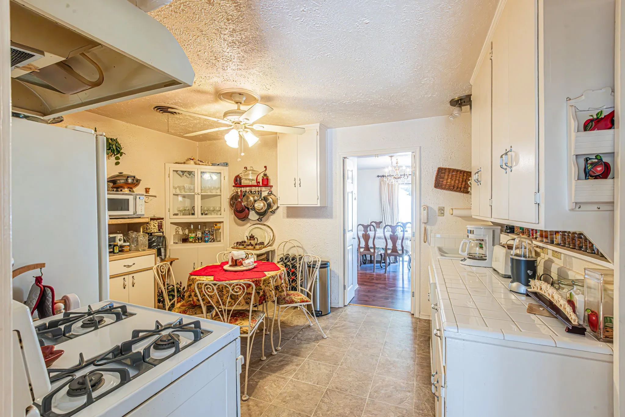 White cabinetry with integrated appliances, tile countertops, and a ceiling fan
