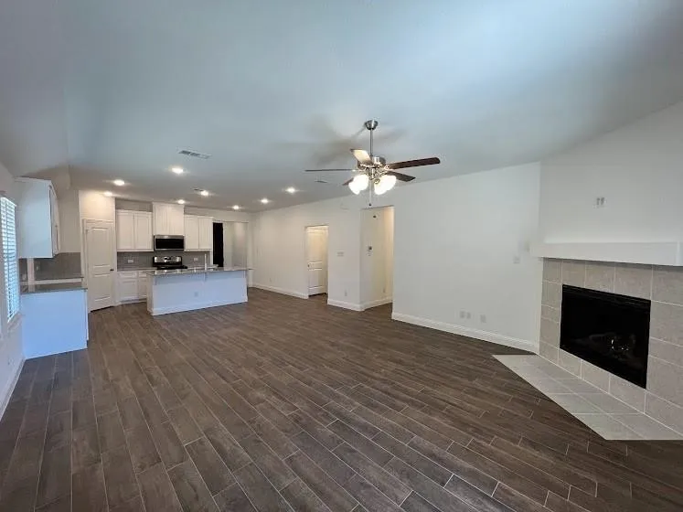 Open-concept living area with wood-finish flooring, a tiled fireplace, and recessed lighting