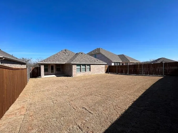 Expansive backyard with a full privacy fence, brick exterior, and covered patio