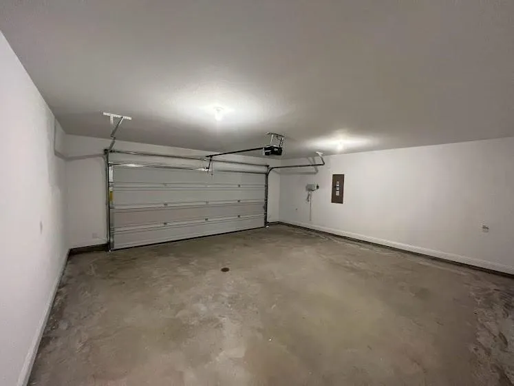 Enclosed garage with a white sectional door, exposed overhead door mechanism, concrete flooring, and ceiling-mounted lighting