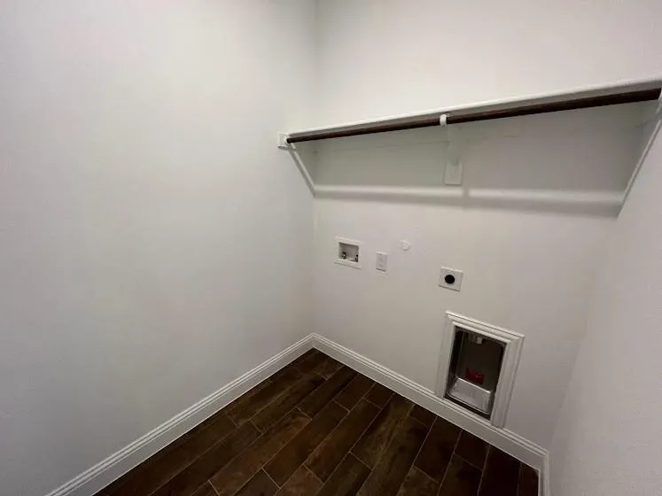 Utility room featuring wood-finish flooring, white painted walls, a pet door opening, electrical outlets, and a retractable drying rack mounted above