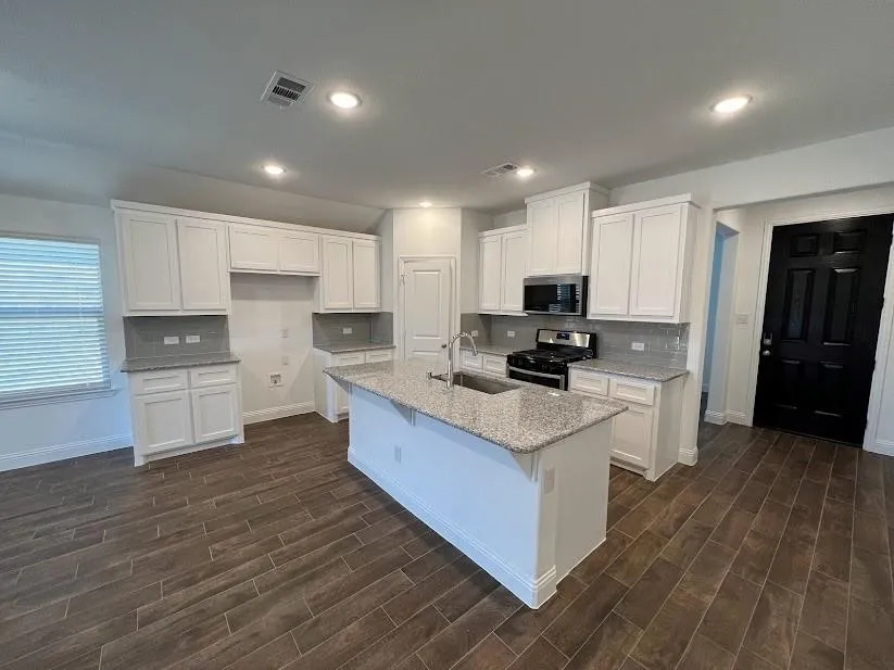 Spacious kitchen featuring white cabinetry, granite countertops, tile backsplash, stainless steel appliances, and a central island with an undermount sink