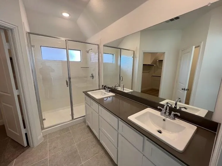Bathroom featuring a double vanity with white cabinetry, dark countertops, and chrome fixtures