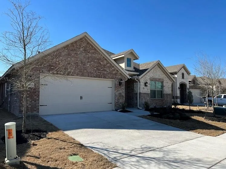 Brick and stone exterior with dormer window accents, attached garage, and concrete driveway