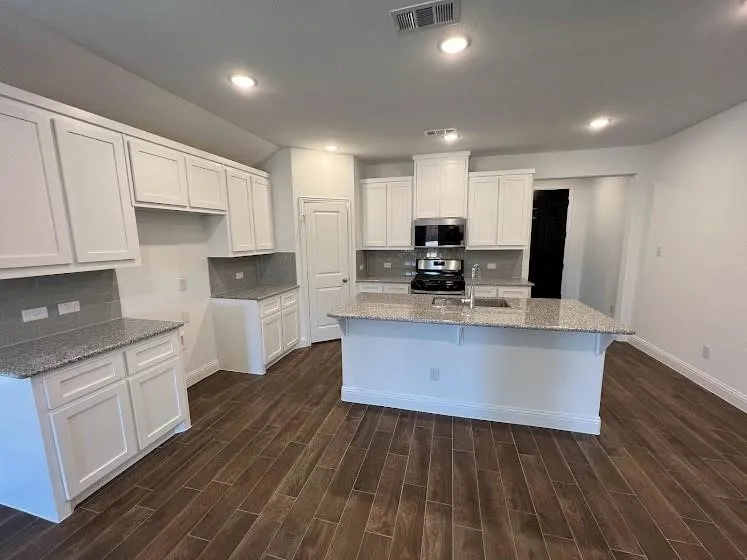Open-concept kitchen featuring white cabinetry, light-toned countertops, a central island with an integrated sink, modern stainless steel appliances, and wood-finish flooring