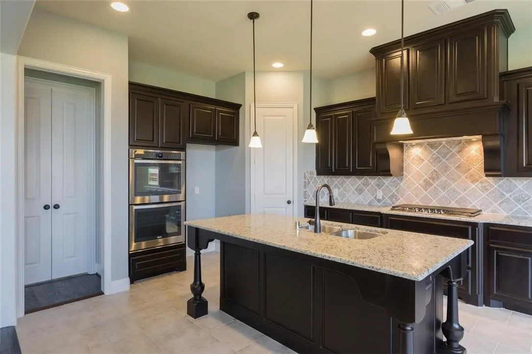 Kitchen featuring appliances with stainless steel finishes, double oven, an island with sink, granite counters, and tile floors