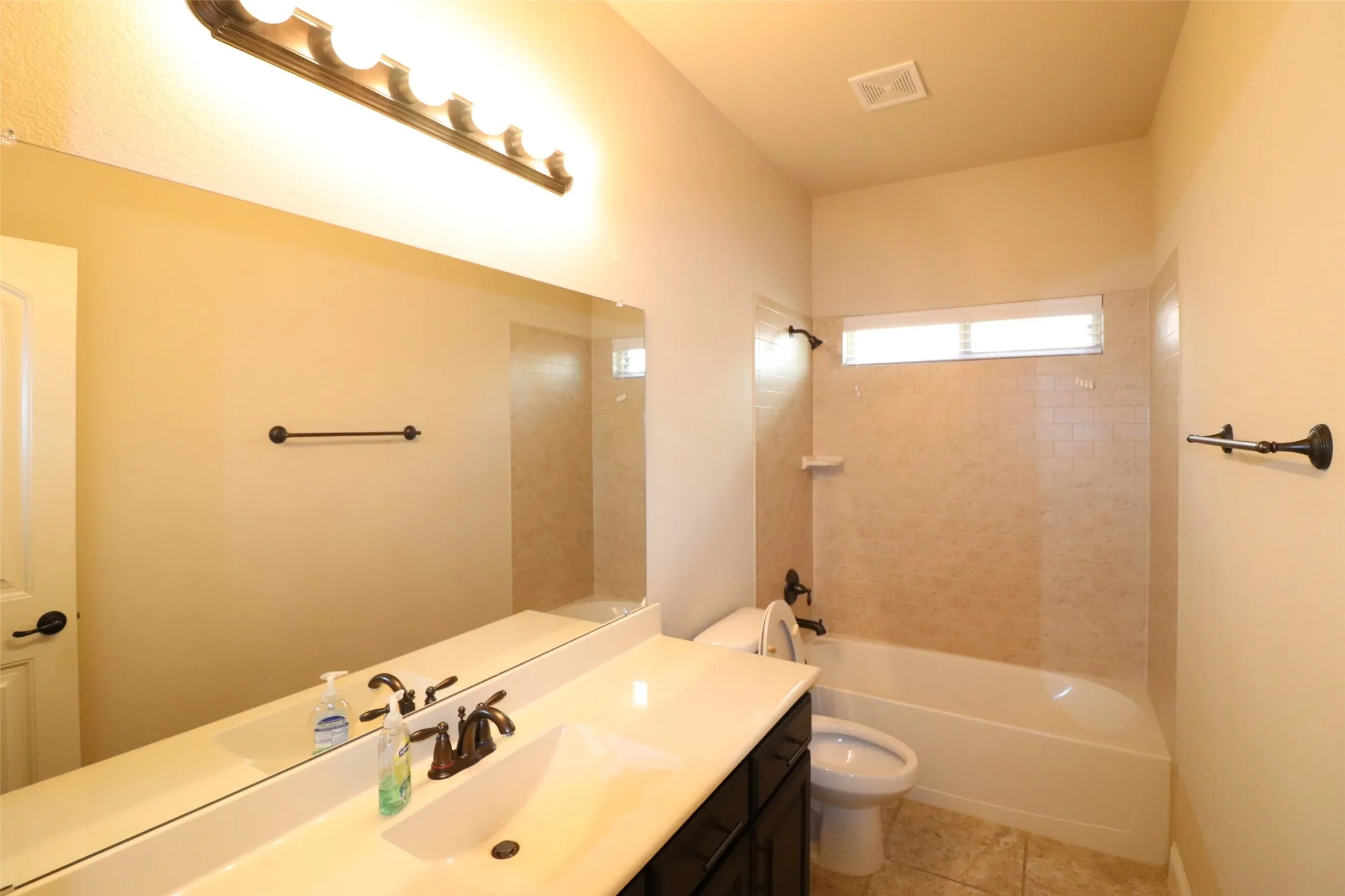 Full-width vanity mirror, dark wood-finish cabinet, white undermount sink, bronze-finish faucet, and tiled shower surround with a built-in bathtub