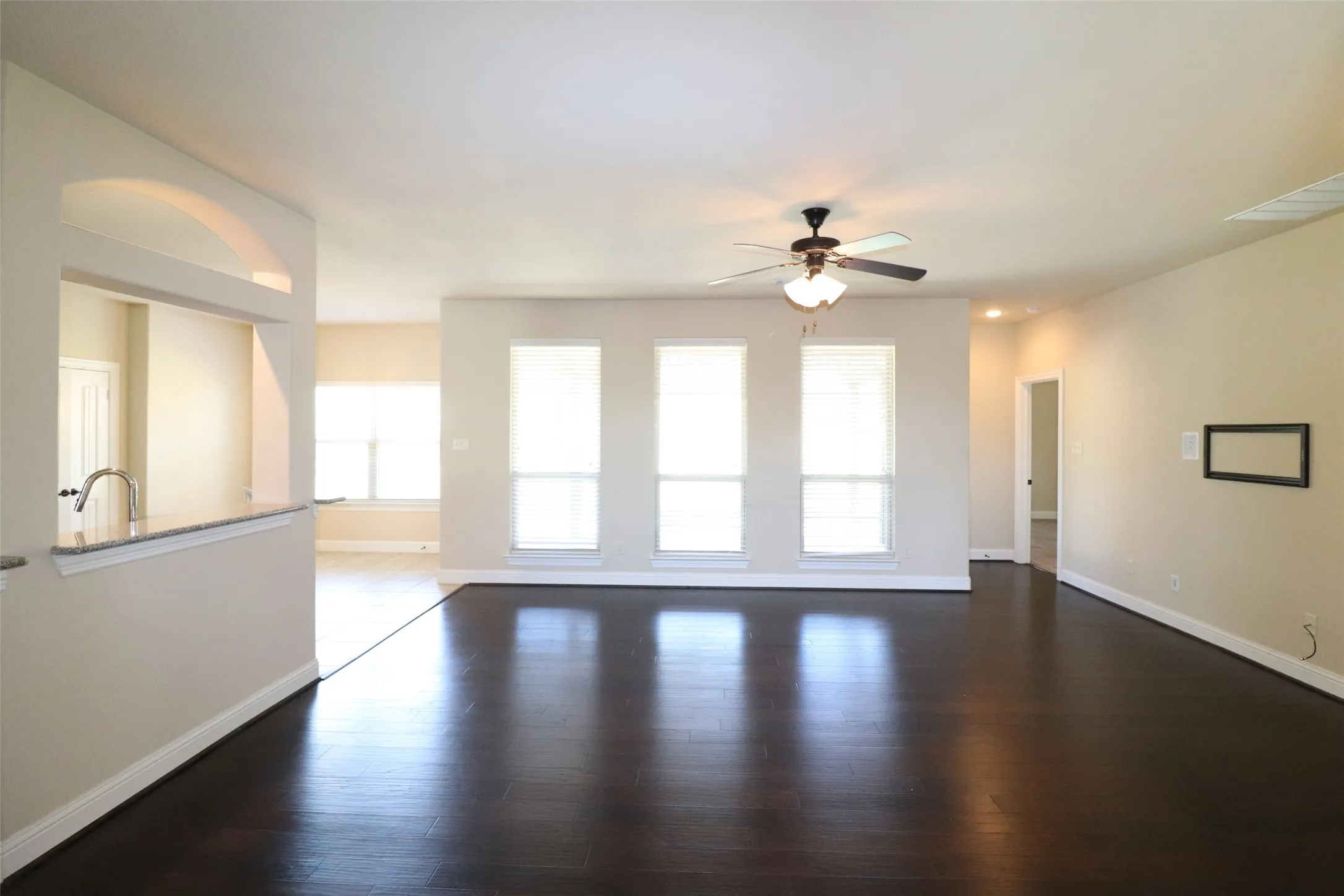 Expansive interior with dark wood-finish flooring, multiple large windows, a built-in ceiling fan, and a pass-through opening with a granite-style countertop