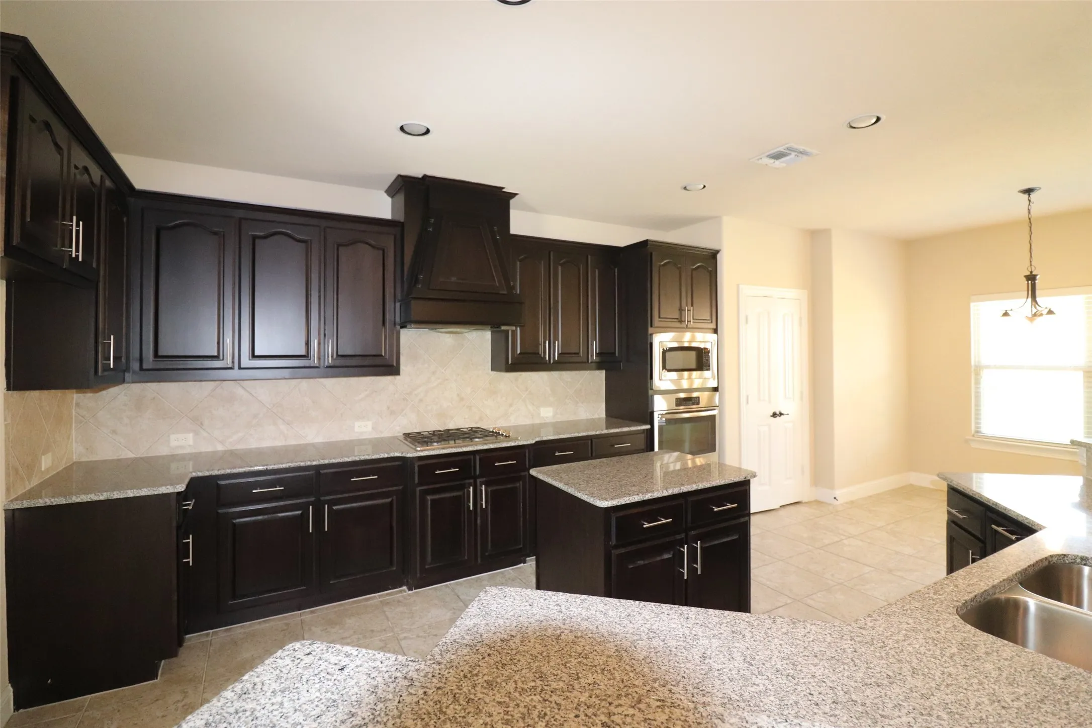 Kitchen featuring dark wood cabinetry, light-toned countertops, a built-in oven and microwave, a dedicated island, and tile flooring