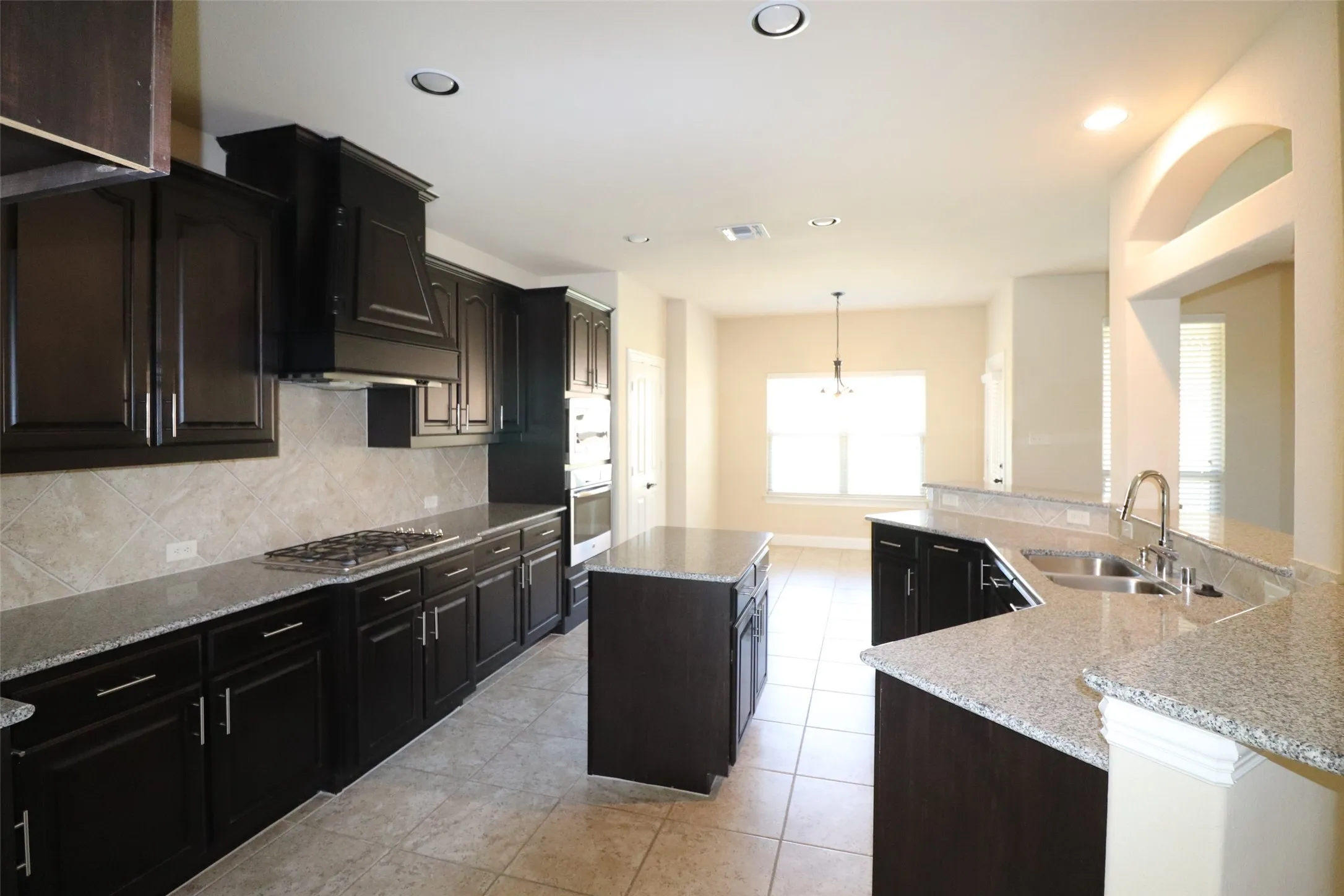 Kitchen featuring dark wood-finish cabinetry, light-toned countertops, a built-in gas range, a stainless steel double basin sink, and recessed lighting