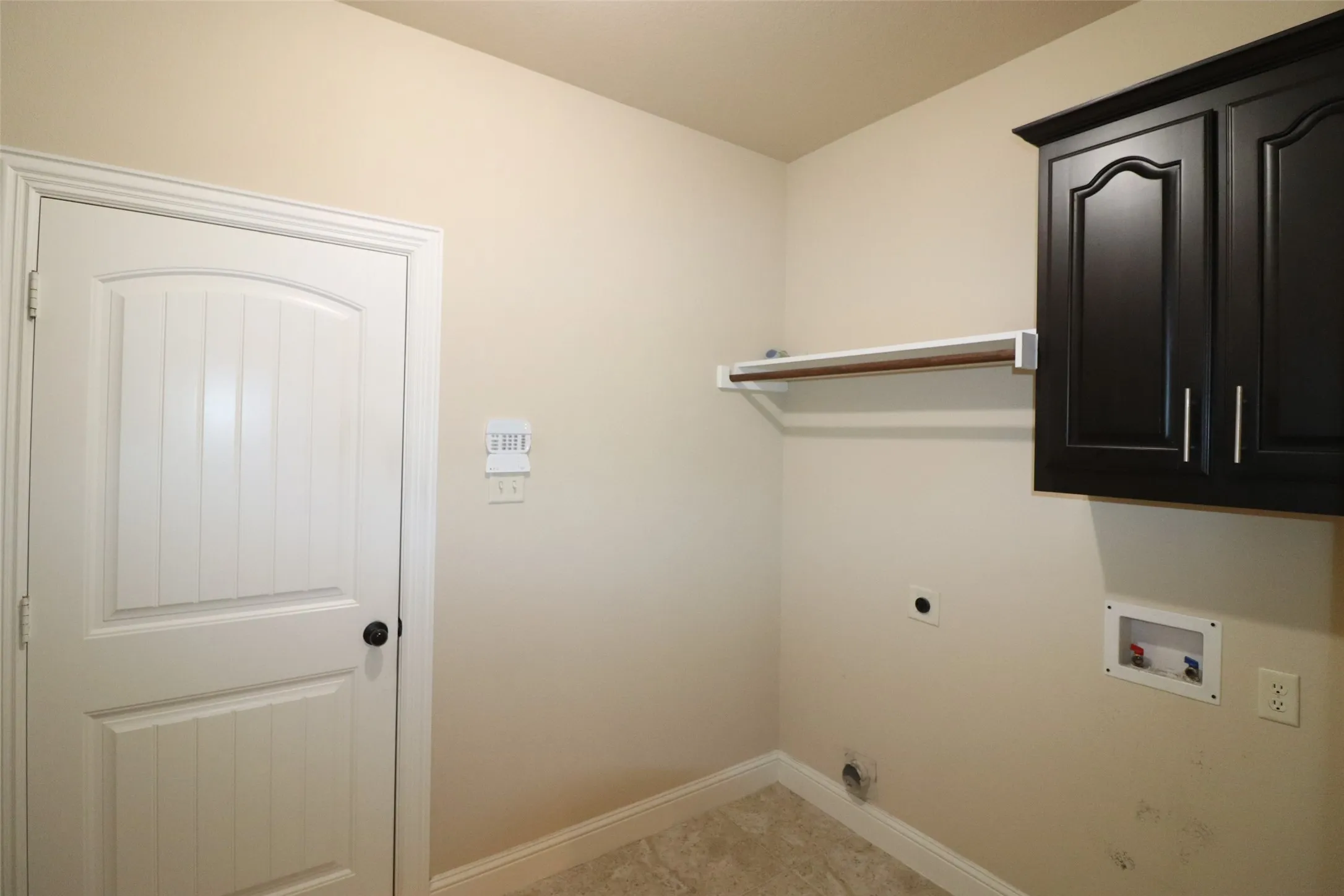 Laundry area featuring dark wood-finish cabinetry, a built-in hanging rod, and light-toned flooring