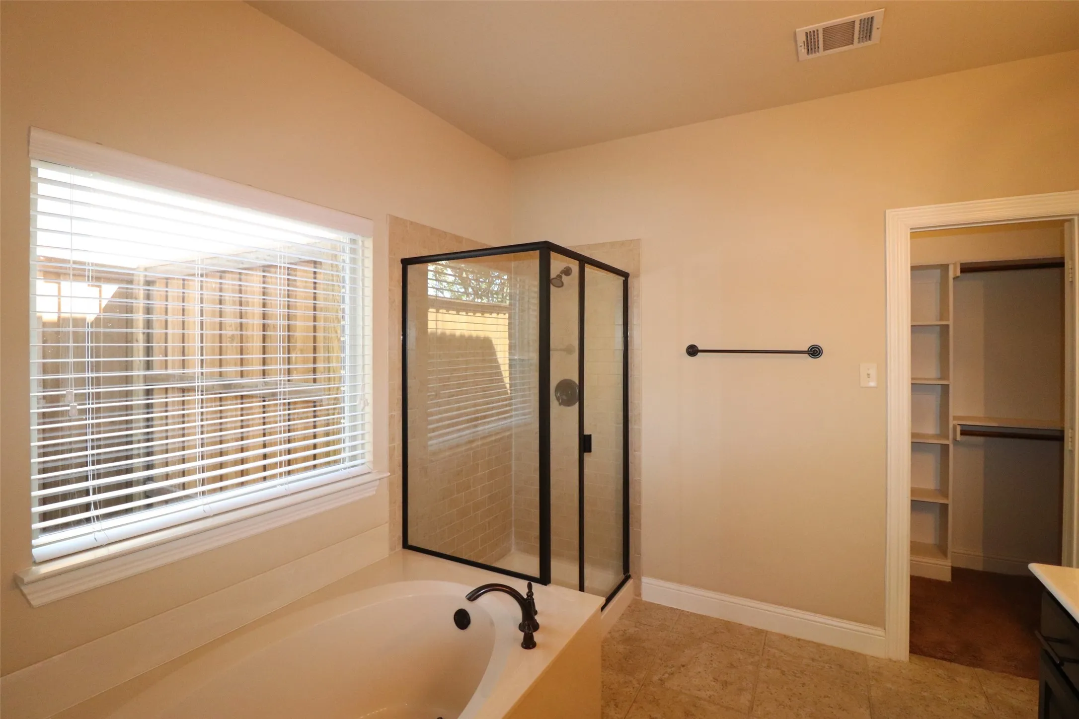 Soaking tub with dark bronze fixtures, framed glass shower enclosure, tile flooring, and a walk-in closet with built-in shelving