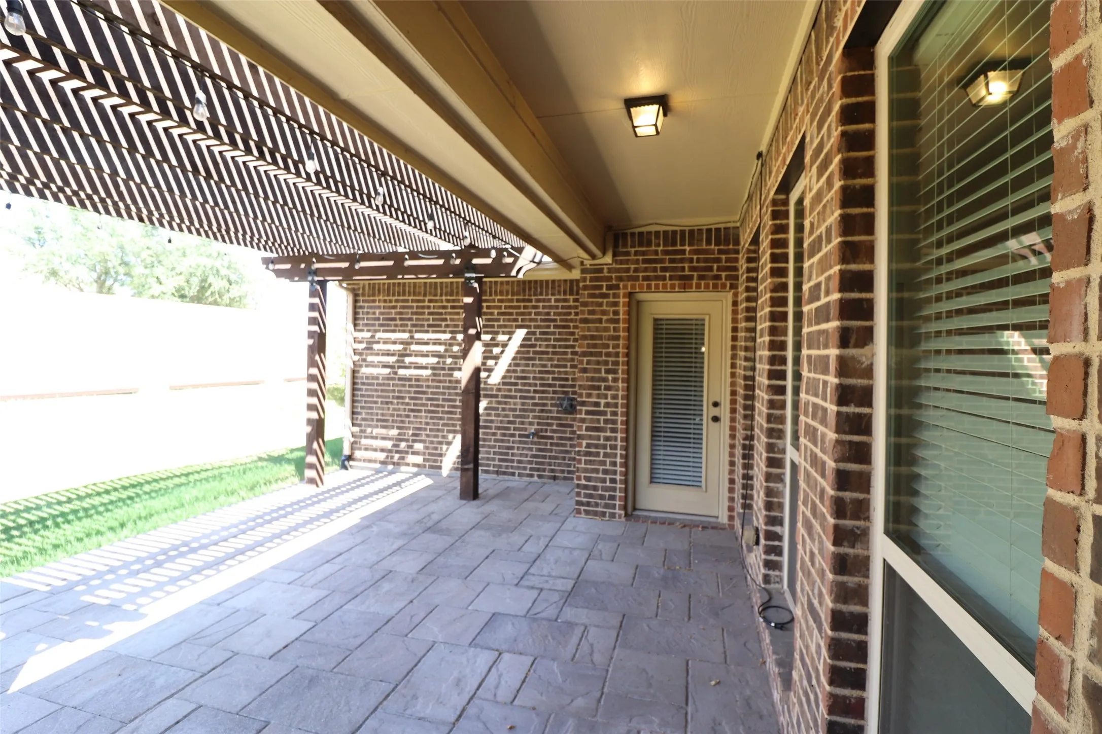 Covered patio with stamped concrete flooring, a decorative wood pergola, and brick exterior walls