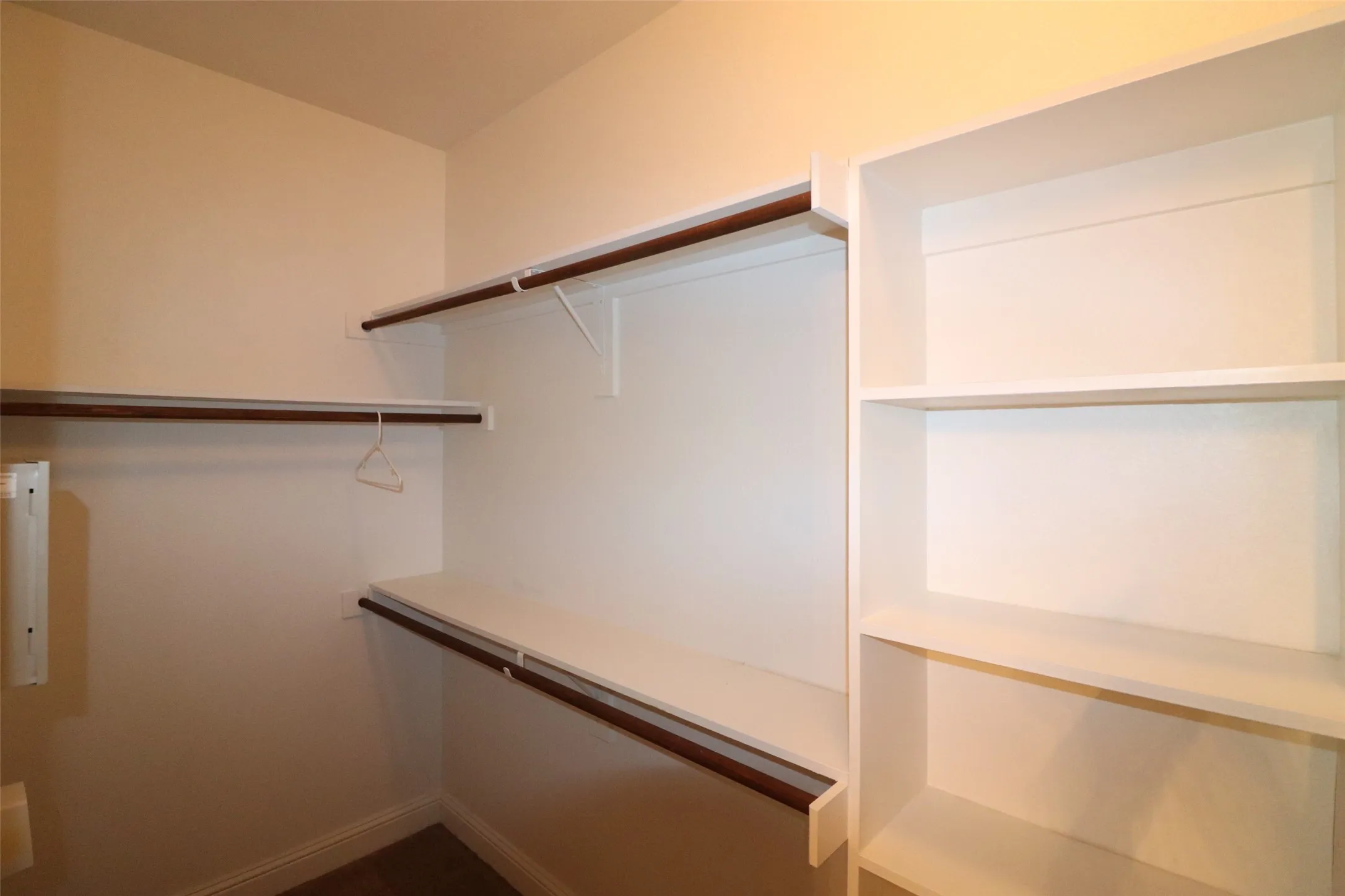 Walk-in closet with built-in shelving, white walls, and wood-finish hanging rods