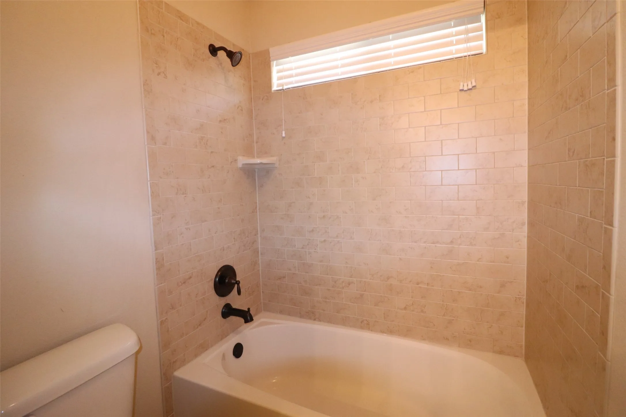 Bathtub with subway tile surround, dark bronze fixtures, and a transom window with blinds