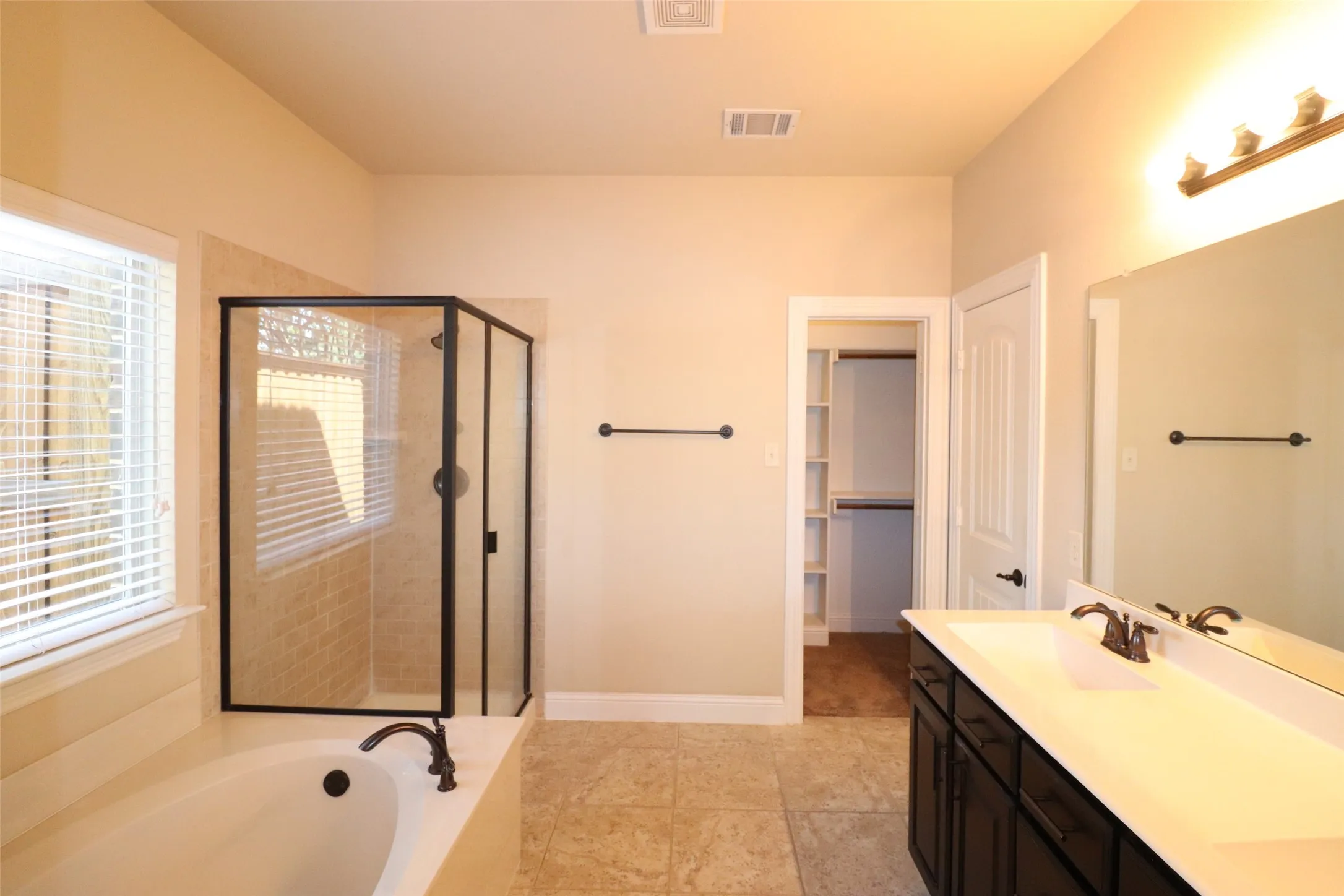 Soaking tub, walk-in shower with clear glass enclosure, vanity with integrated sink, rectangular mirror, and tile flooring