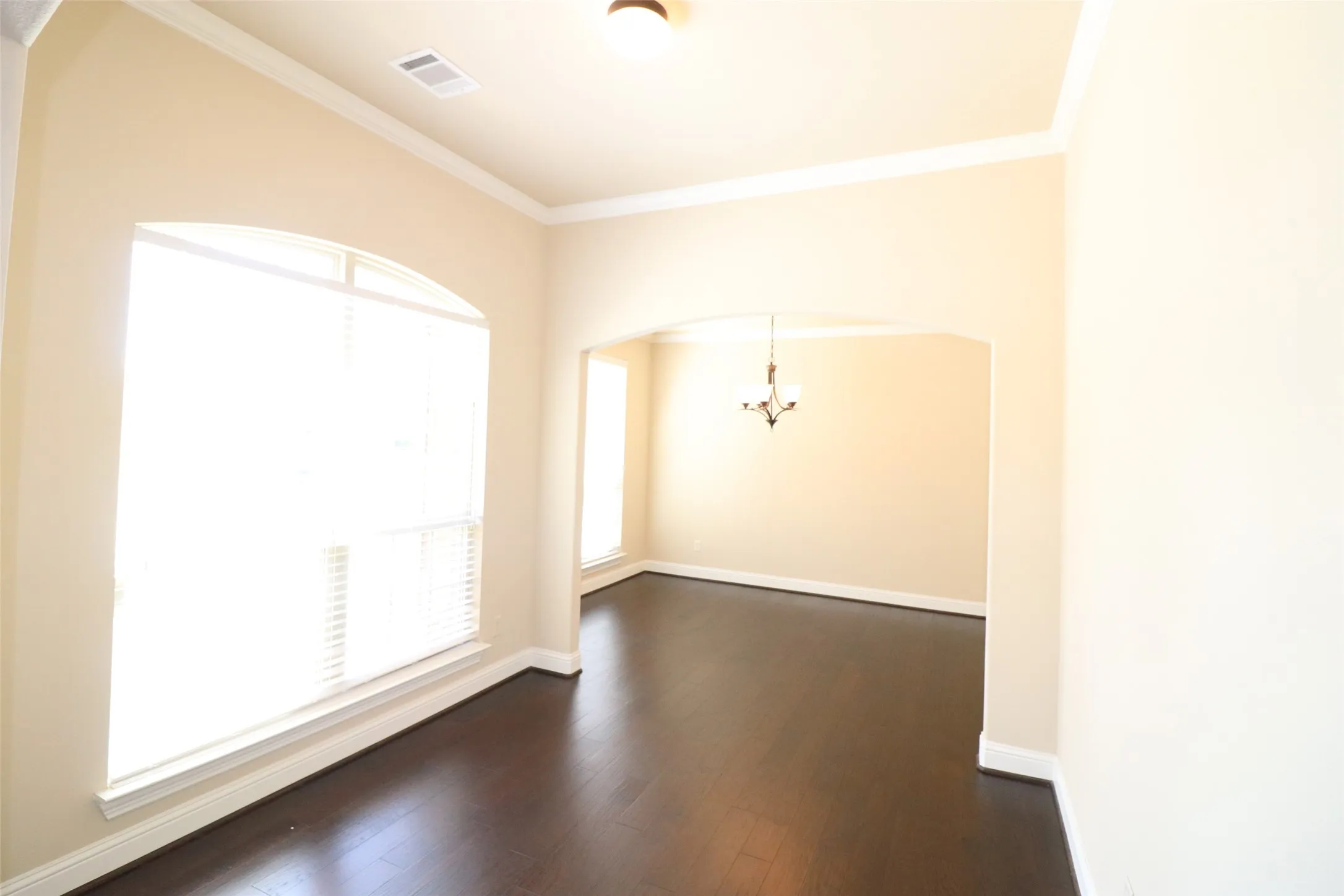 Recessed ceiling with crown molding, dark wood-finish flooring, arched doorway, and a traditional chandelier