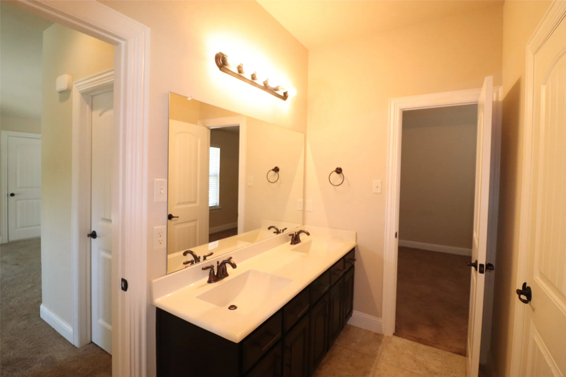 Dual vanity with integrated sinks, white countertop, dark wood-finish cabinetry, and a large wall-mounted mirror