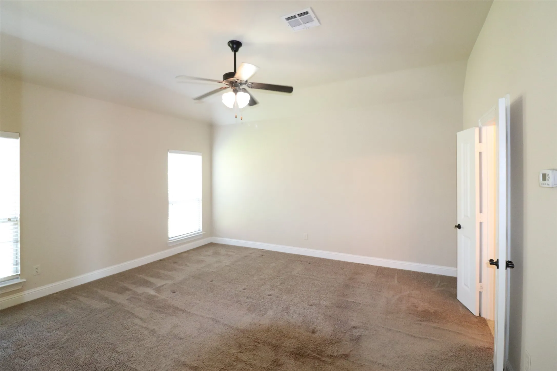 Vaulted ceiling with a ceiling fan light fixture, two windows, carpeted flooring, and a white paneled door with black hardware