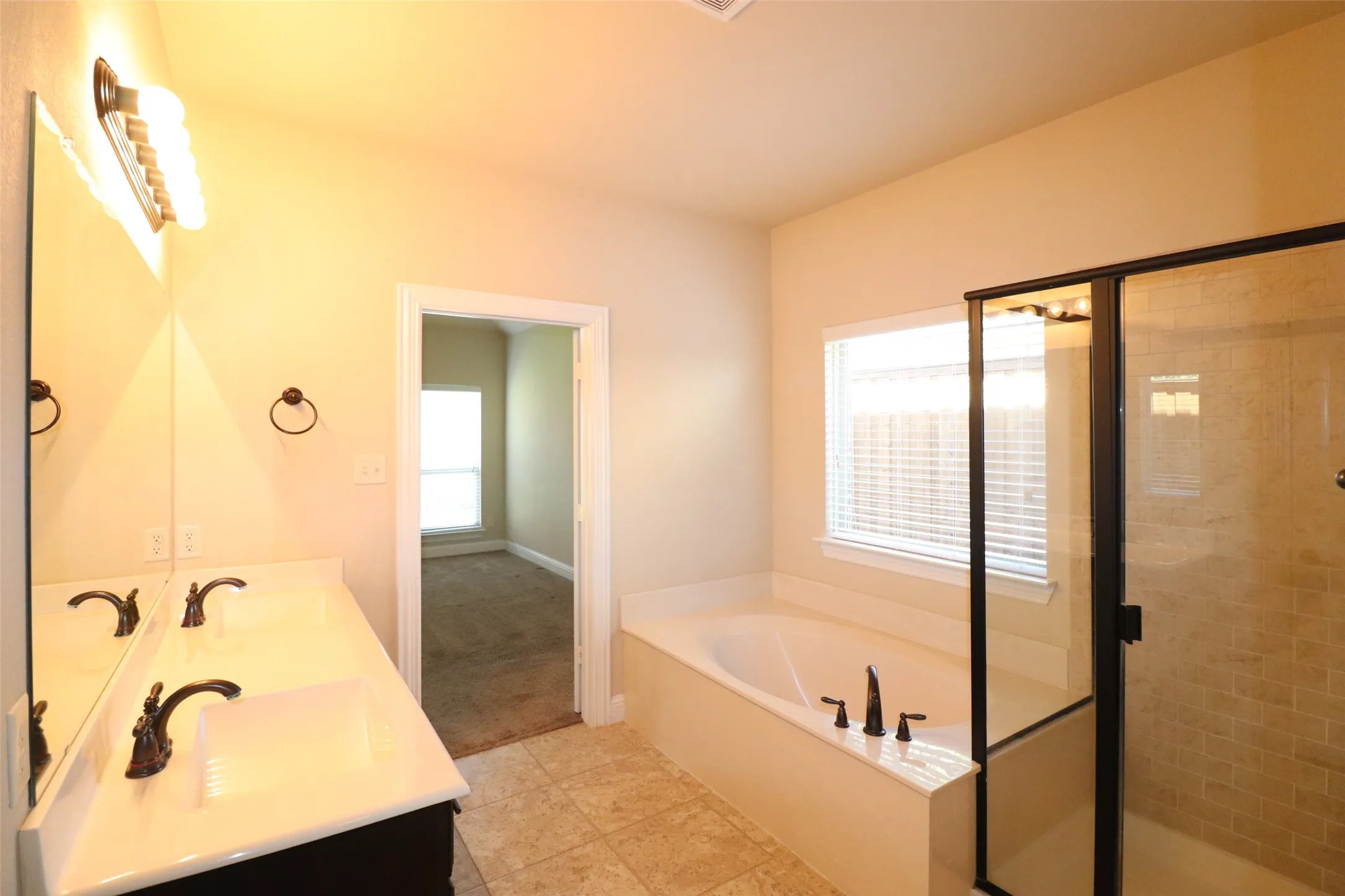 Dual vanity with integrated sinks, framed mirror, built-in bathtub, glass-enclosed shower, and tiled flooring