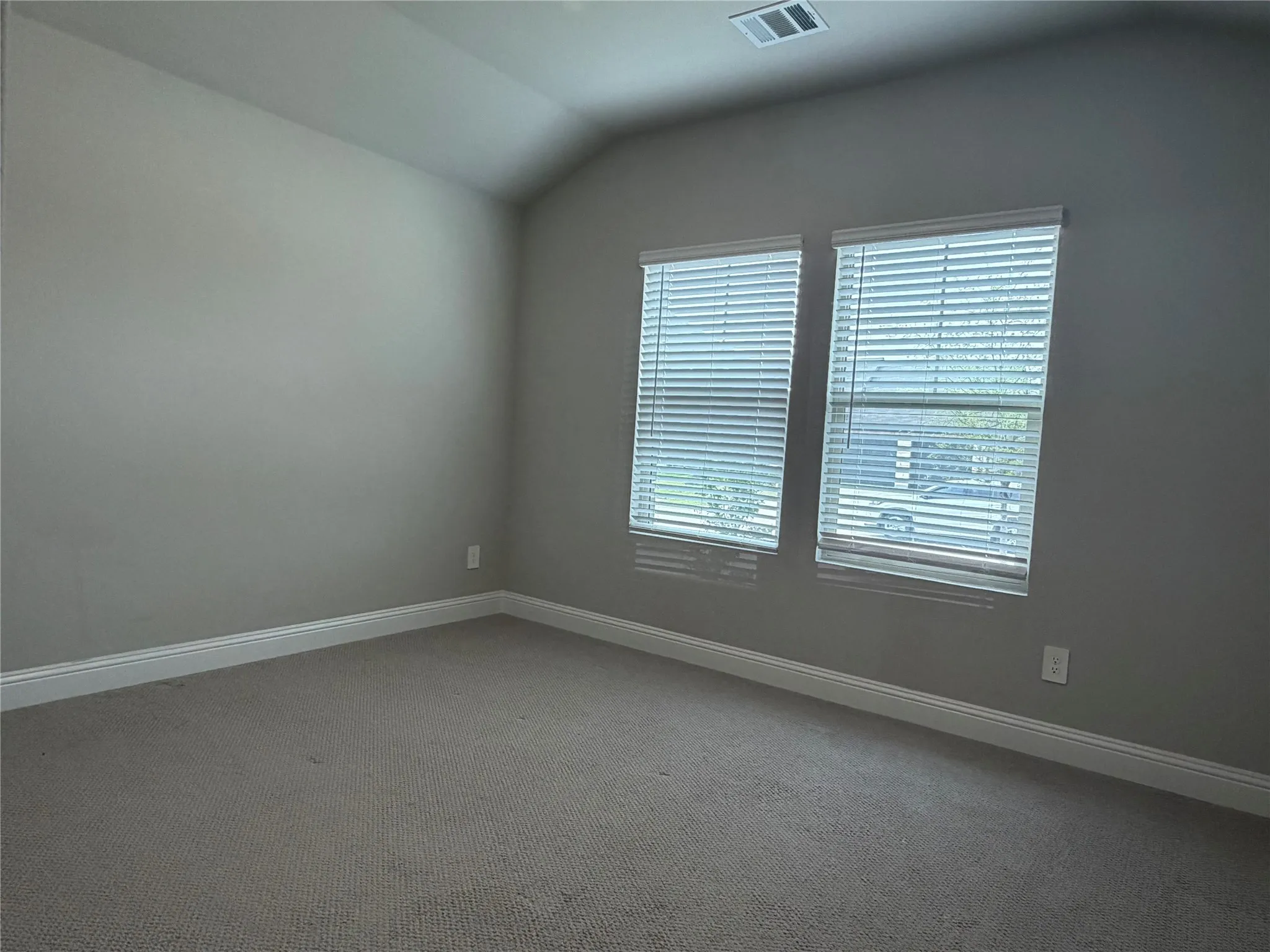 Vaulted ceiling, two windows with blinds, carpeted flooring, and light gray wall paint