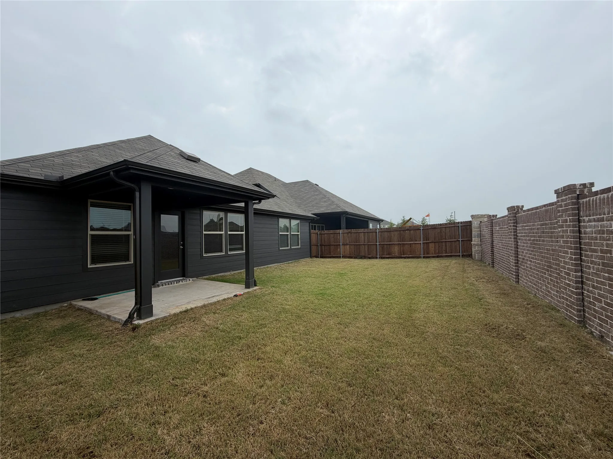 Expansive backyard featuring a brick privacy wall, wood privacy fencing, and a covered concrete patio
