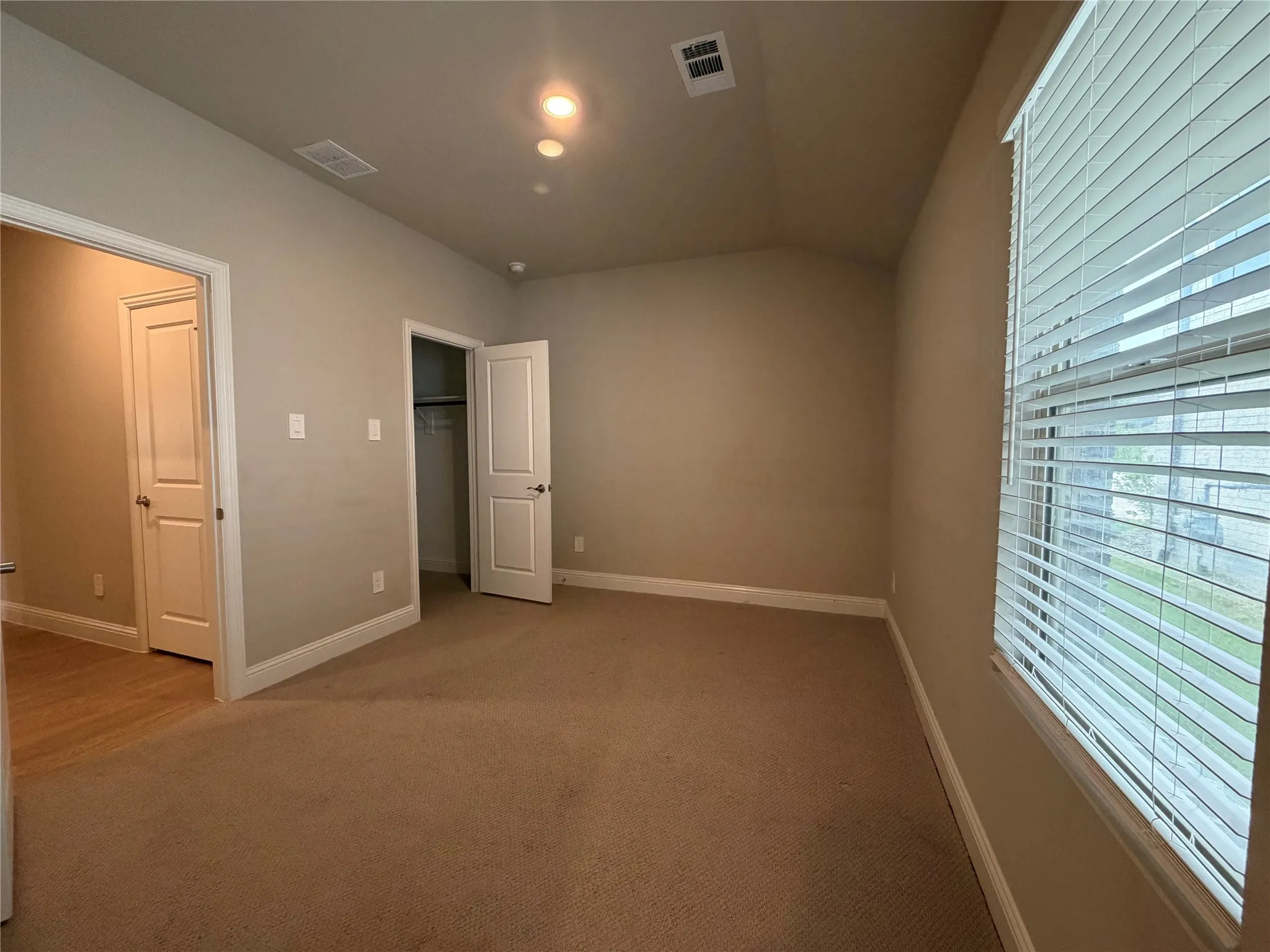 Carpeted room with vaulted ceilings, recessed lighting, and a window with horizontal blinds