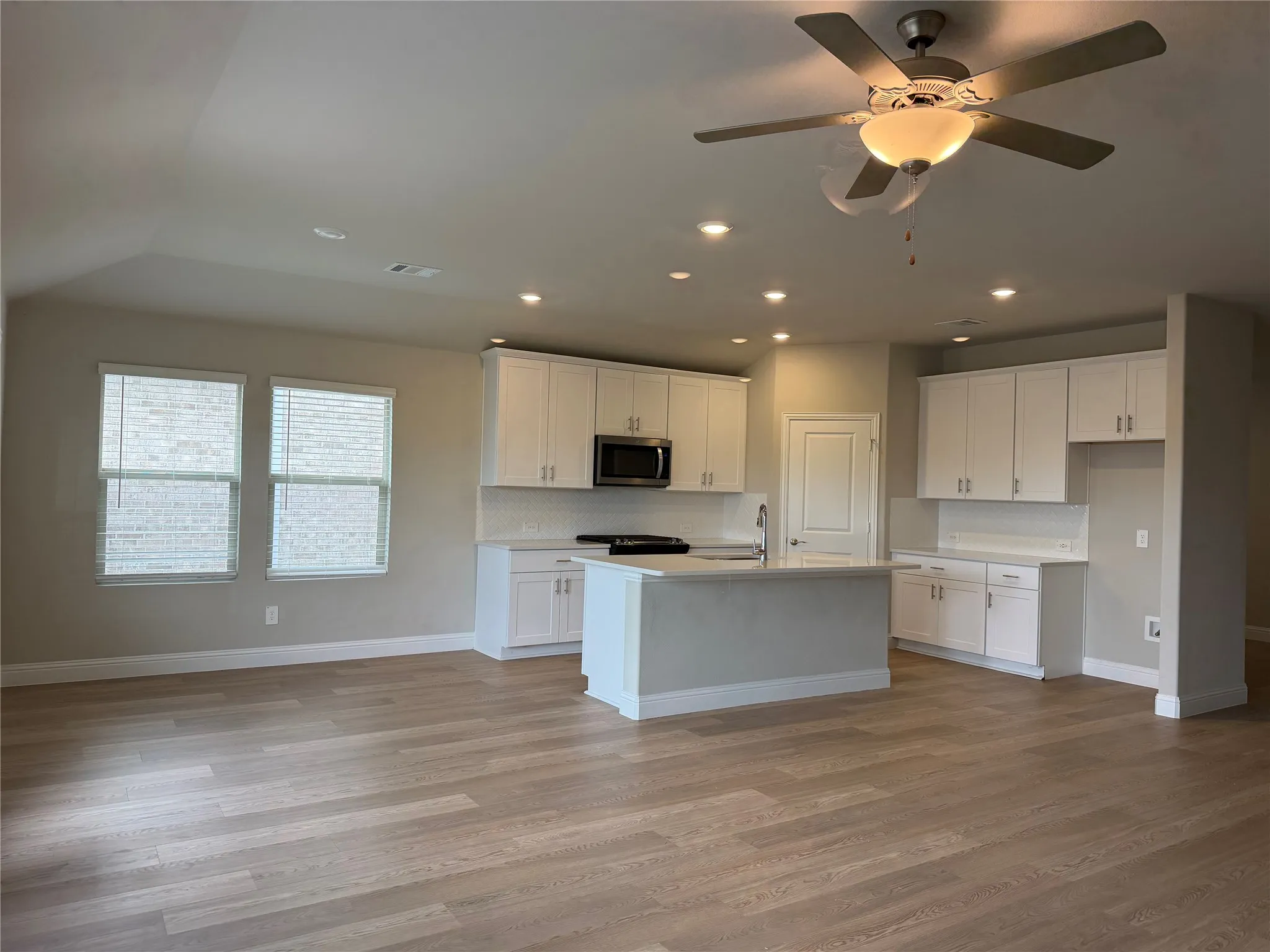 Open-concept kitchen with white cabinetry, stainless steel microwave, light-toned backsplash, and a central island with sink