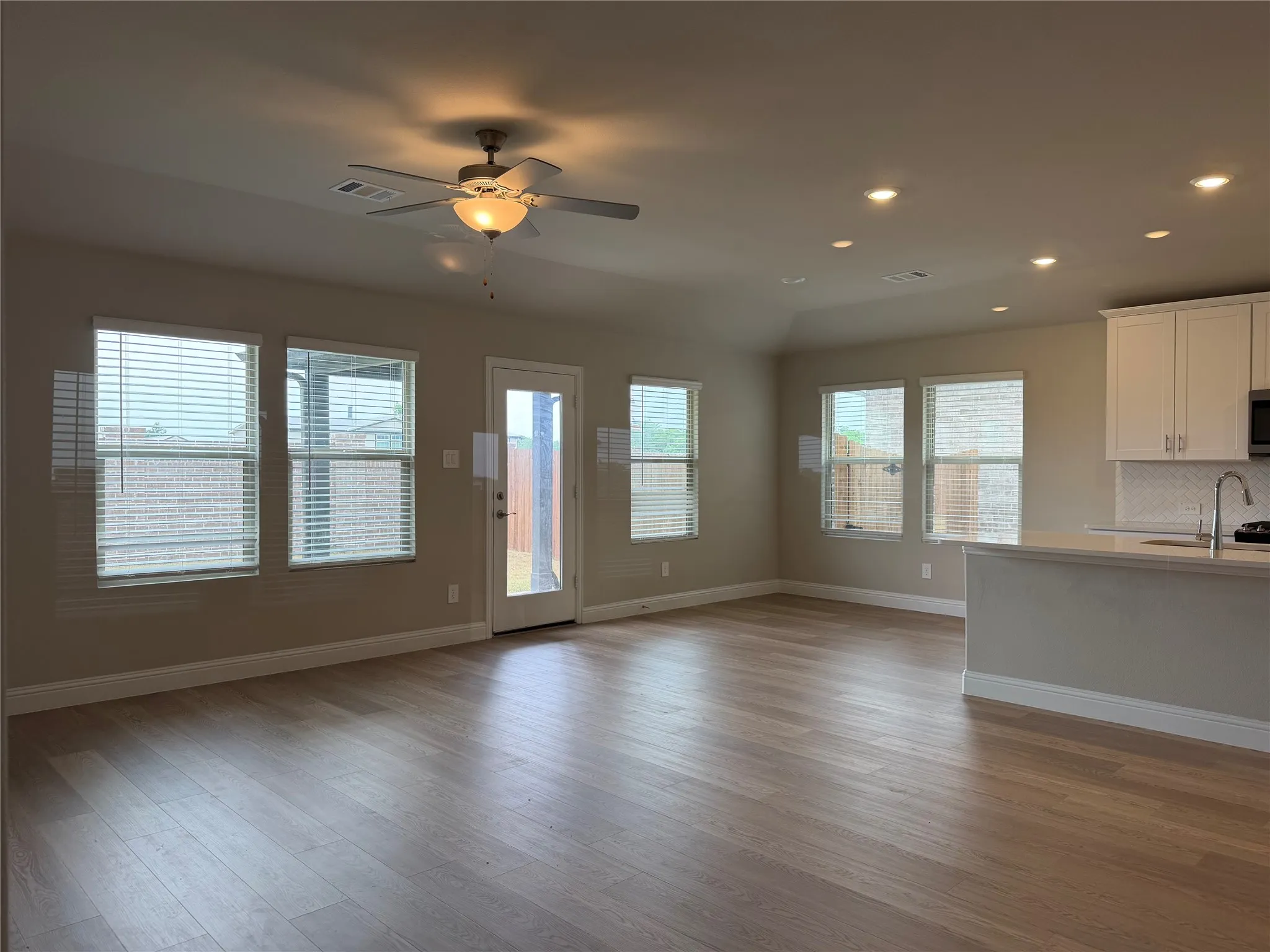 Spacious room featuring wood-finish flooring, multiple windows with blinds, a ceiling fan, and recessed lighting