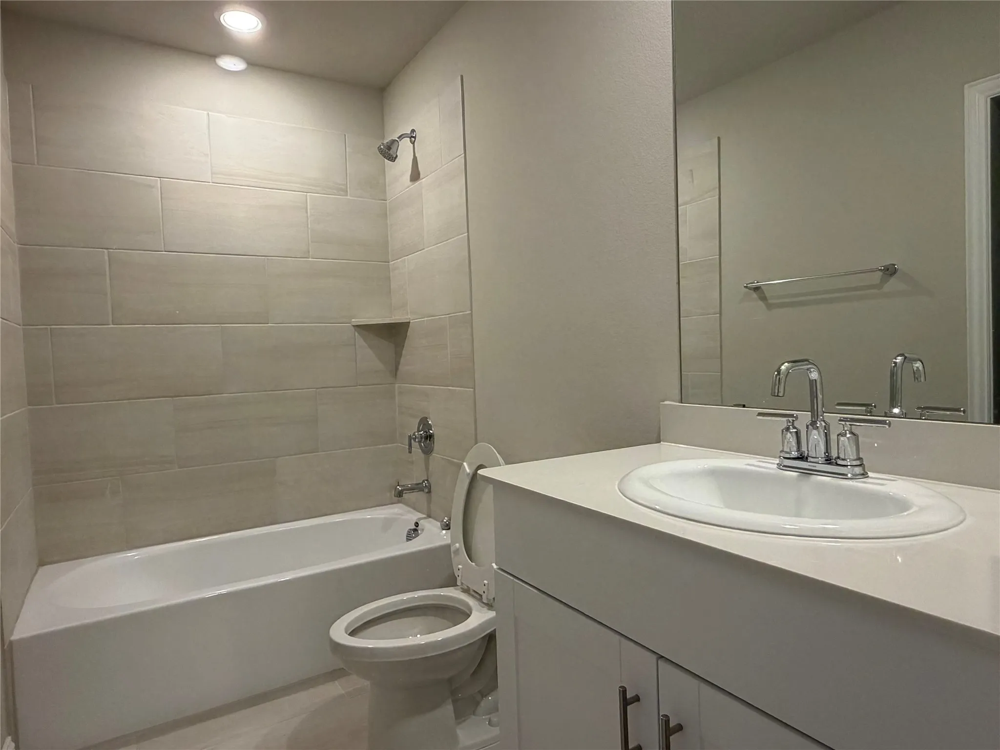 Full bathroom featuring a single vanity with an integrated sink, a built-in bathtub with a shower, and a tiled shower surround with an integrated shelf