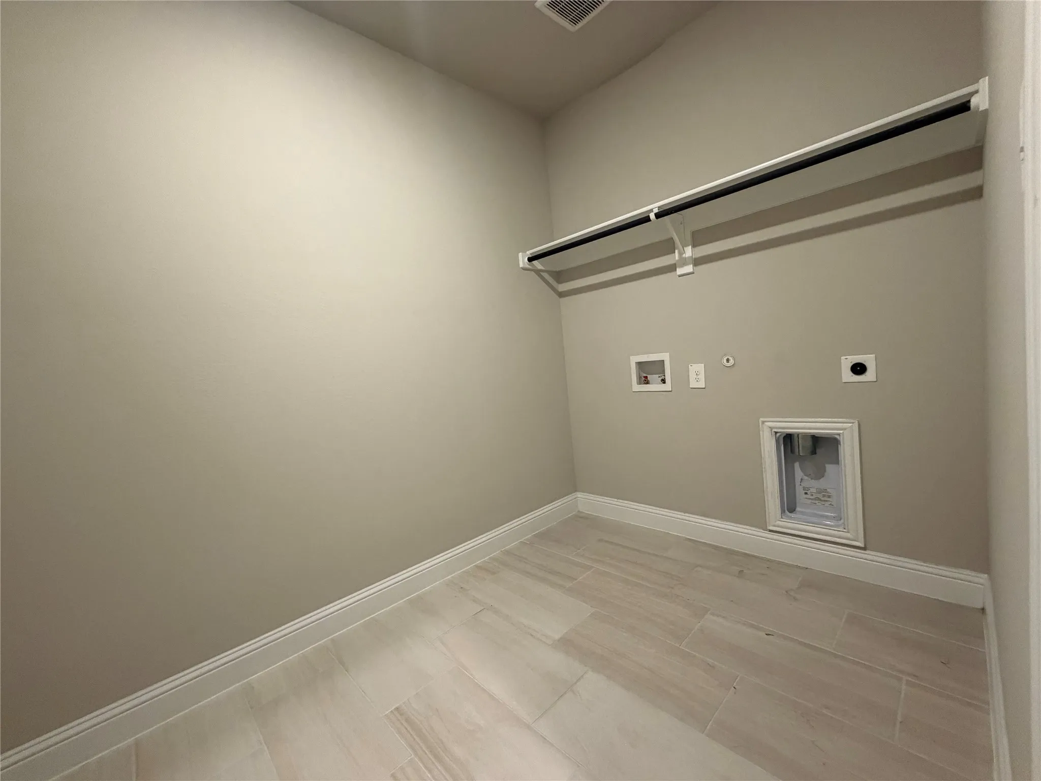 Utility room featuring tile flooring, neutral wall tones, white trim, and a wall-mounted hanging rod
