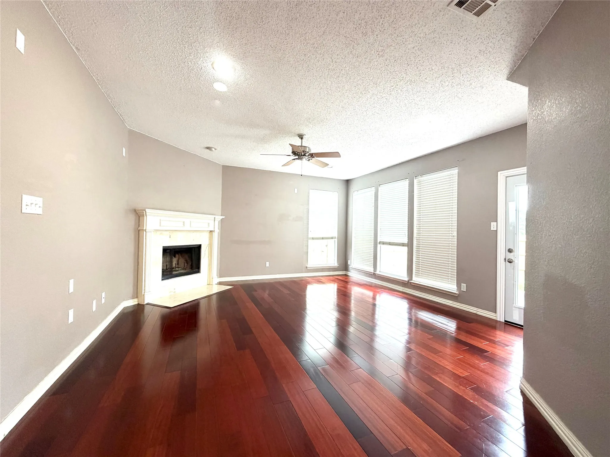 Hardwood flooring, fireplace with mantel, ceiling fan, multiple windows with blinds, and a glass-paneled door
