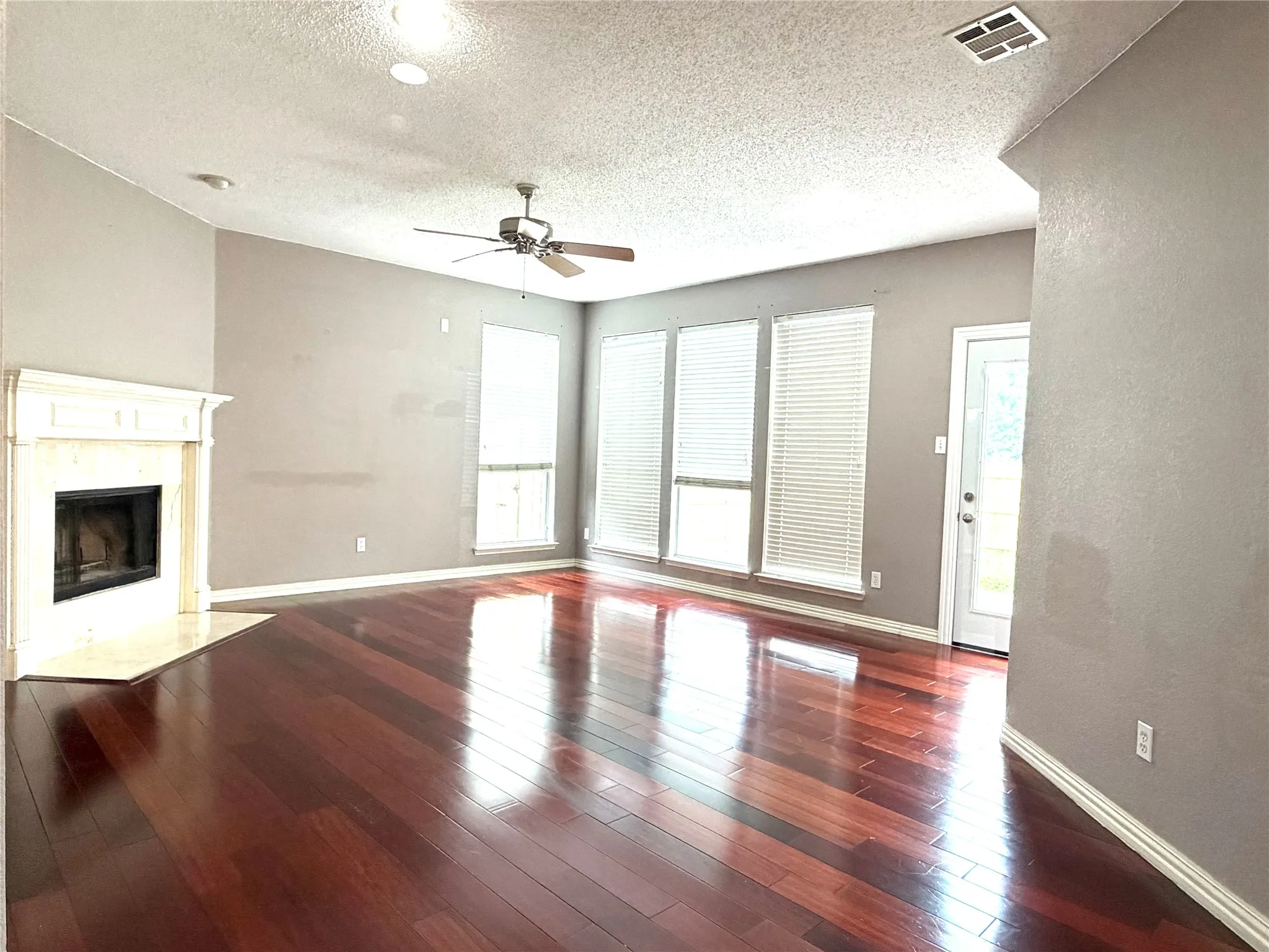 Living area with wood-finish flooring, a white mantel fireplace, and a ceiling fan
