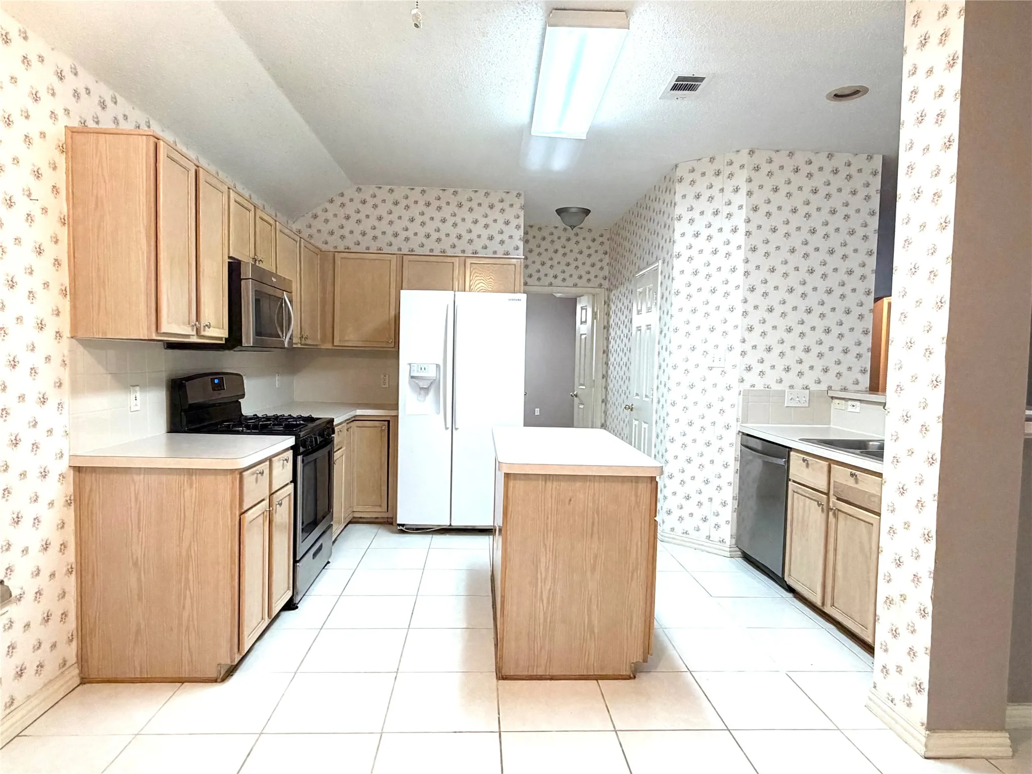 Kitchen featuring light wood-finish cabinetry, white tile flooring, white countertops, and a central island