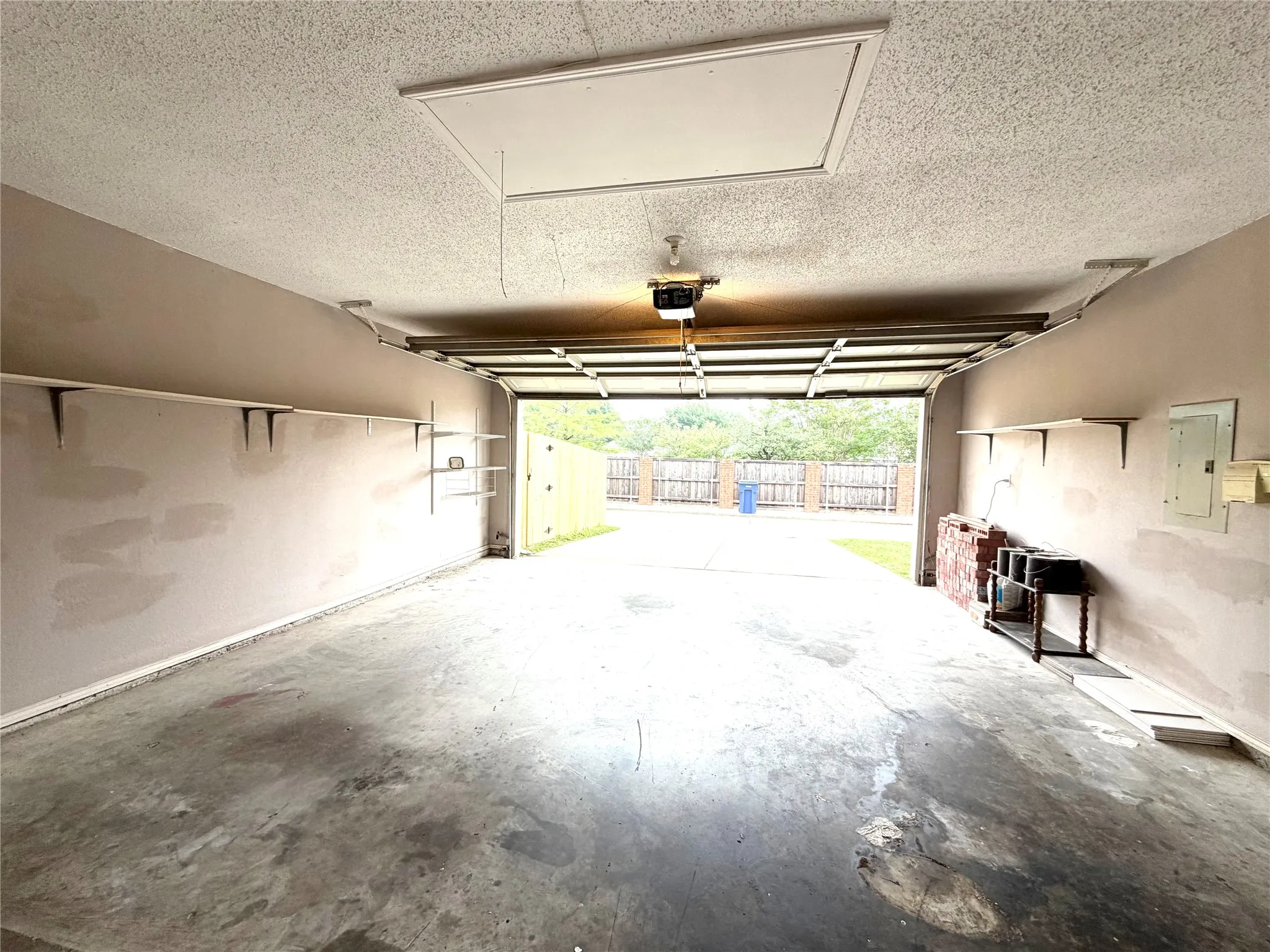Attached garage with concrete flooring, wall-mounted shelving, and a textured ceiling