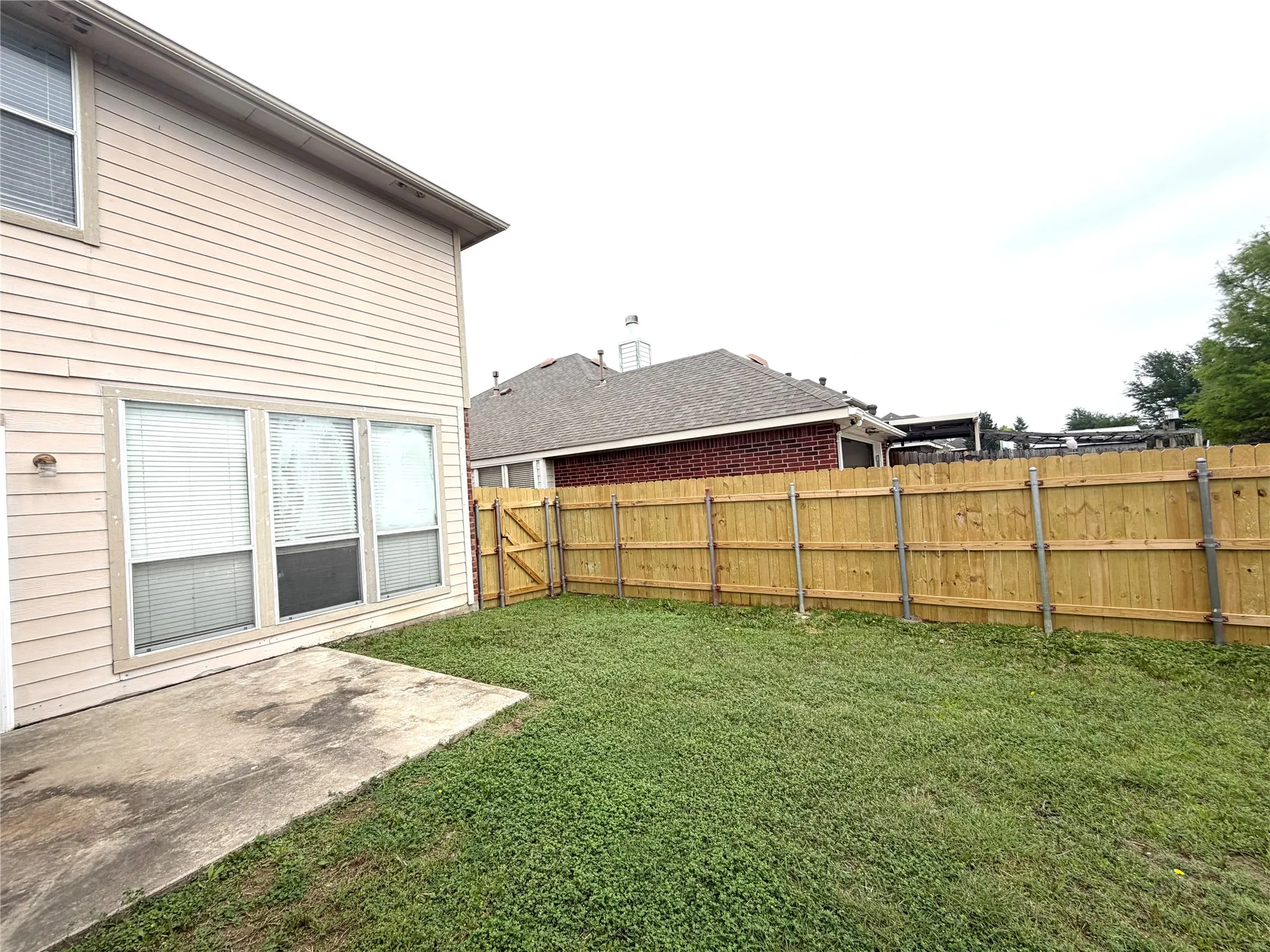 Private backyard featuring wood panel fencing with a gate, a concrete patio, and mature lawn